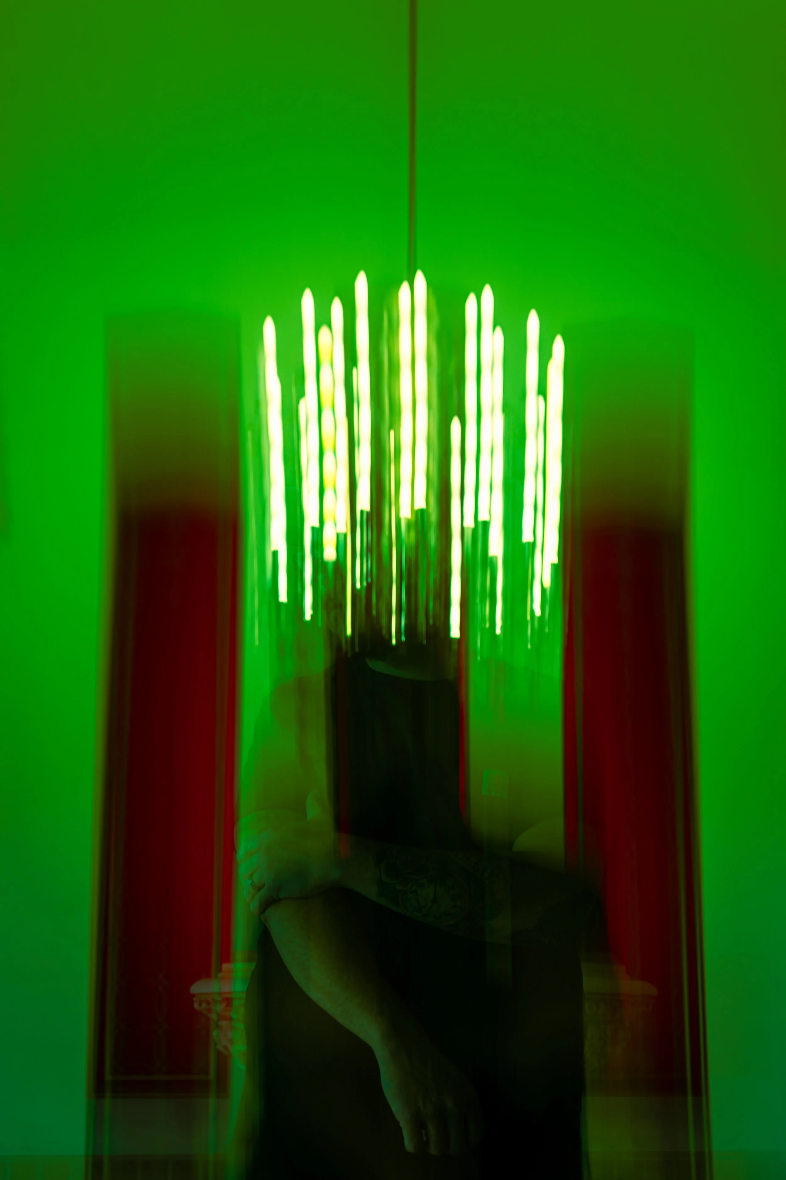 A person taking a selfie in a mirror, captioned with capturing photo of a bright green chandelier against a green wall, with red curtains on sides.