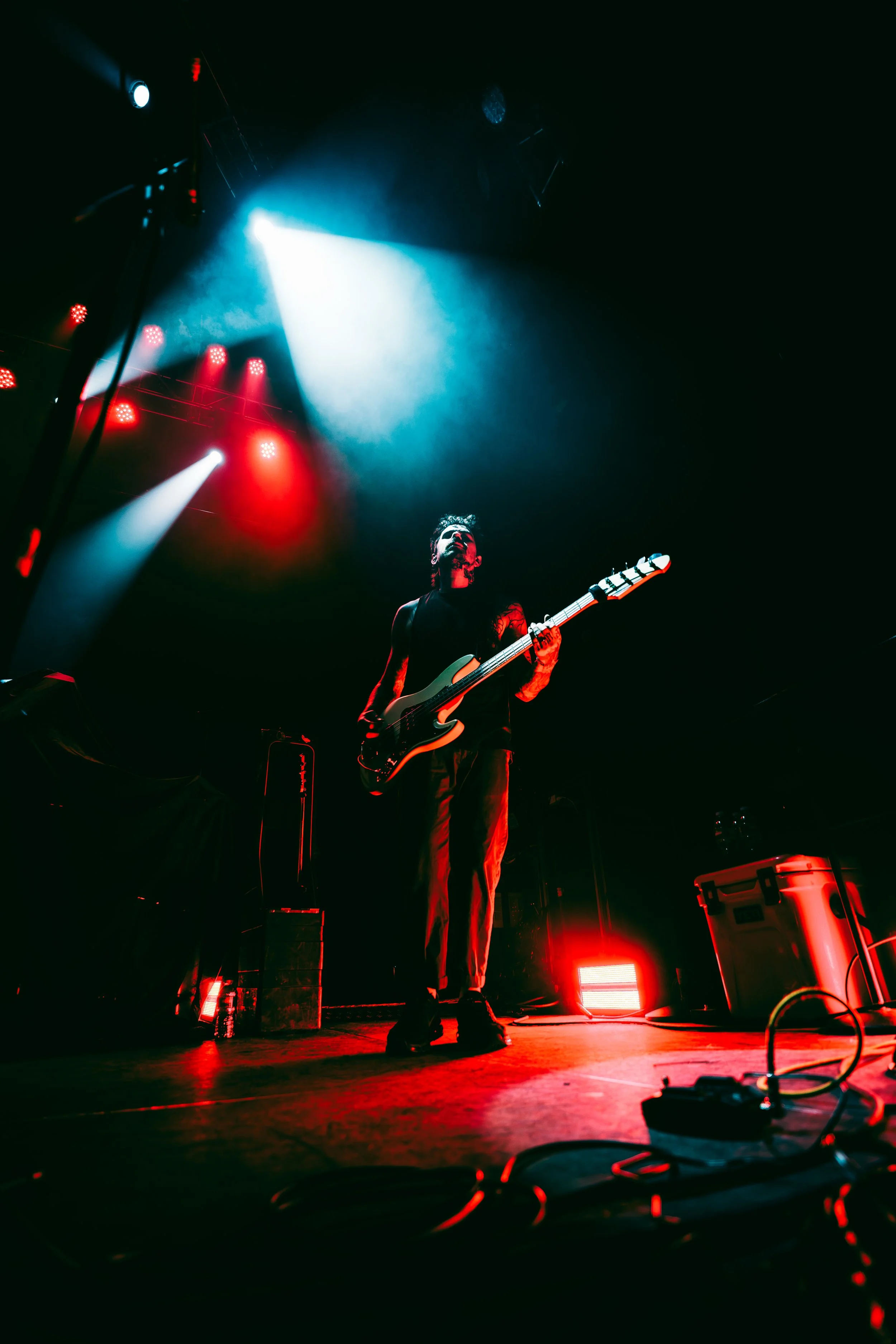 A musician playing an electric guitar on stage under colorful red and blue lights during a live concert.