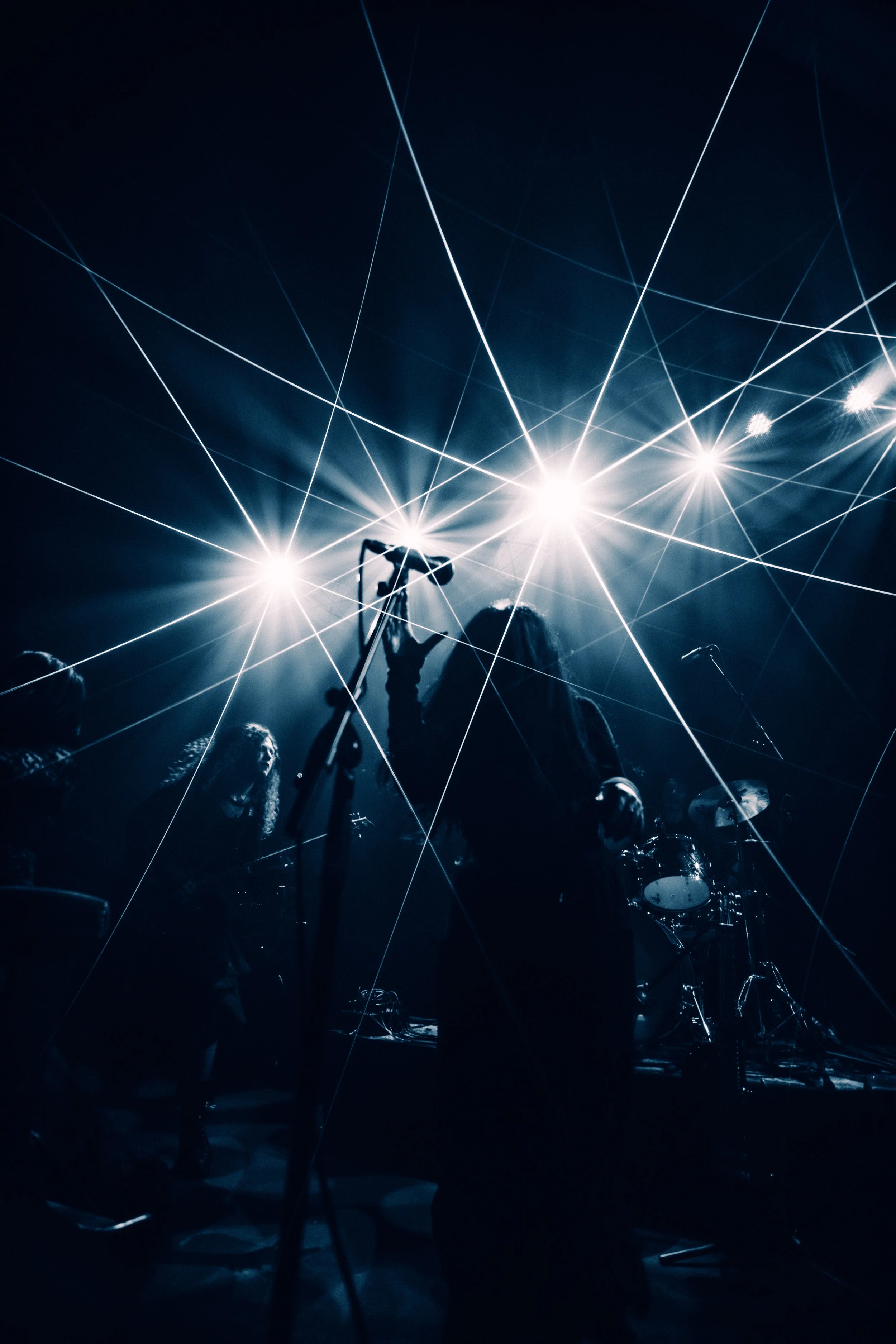 Silhouettes of a band performing on stage with bright lights and laser effects.