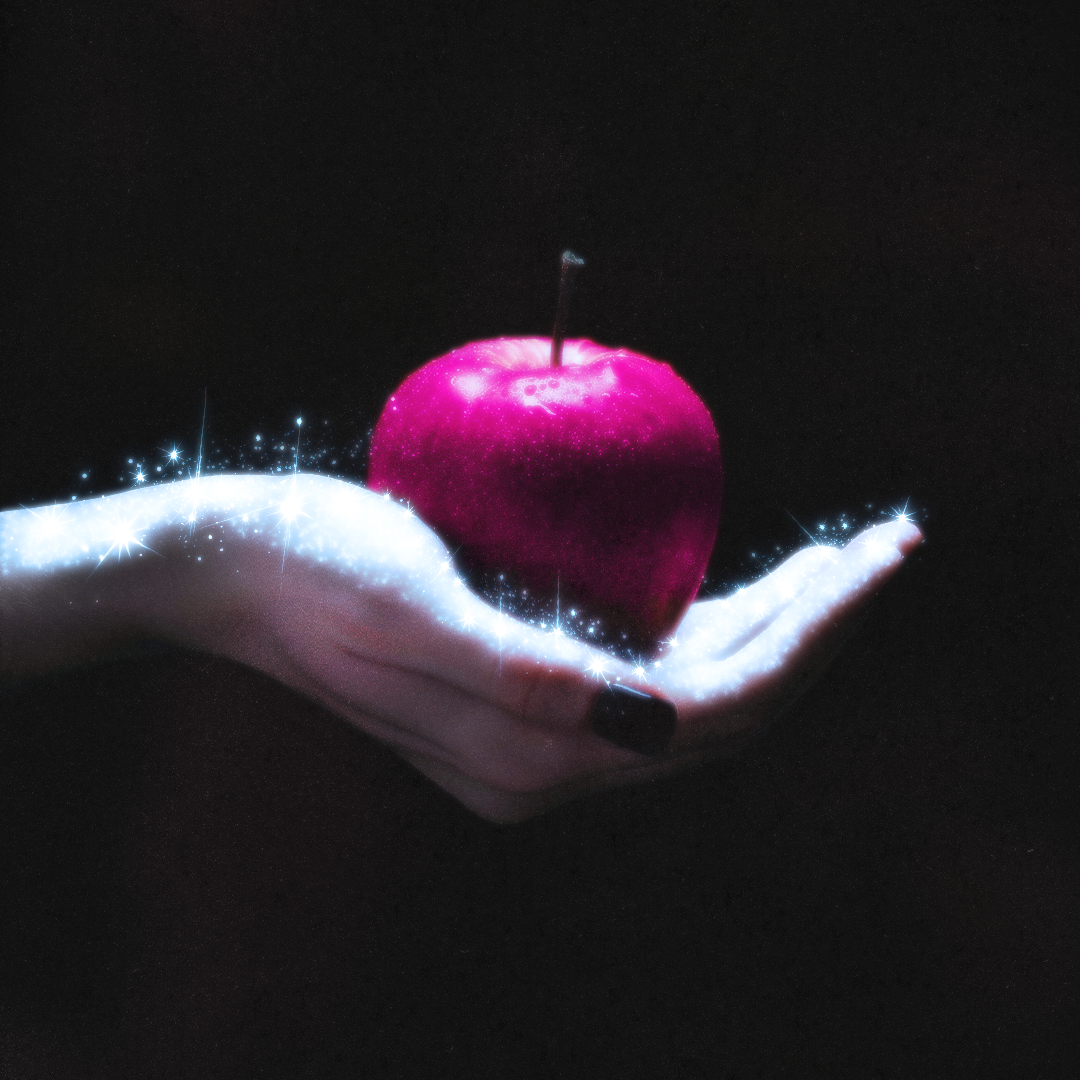 A hand with black nail polish holding a sparkling, glowing red apple against a black background.