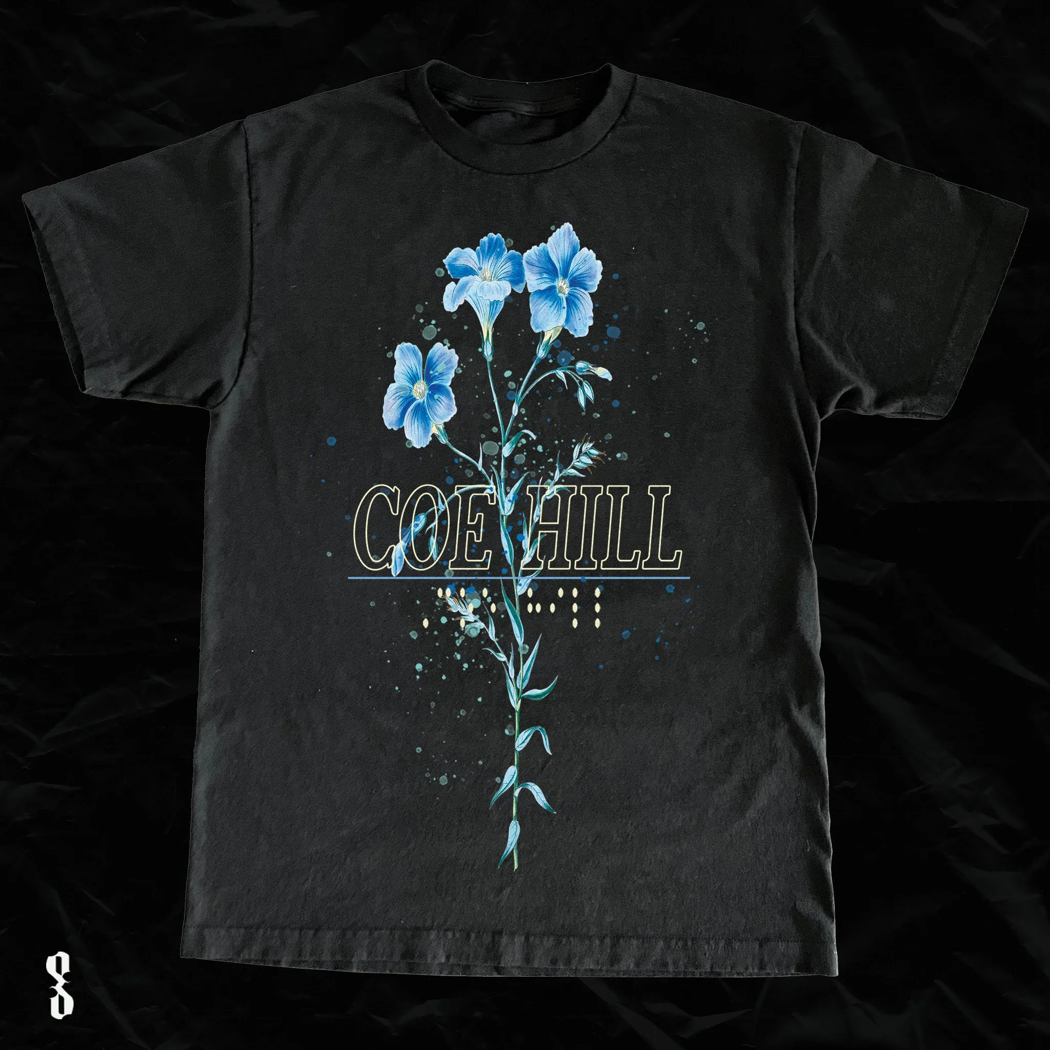 Black T-shirt featuring a blue floral design with the name 'Coe Hill' printed across the flowers.