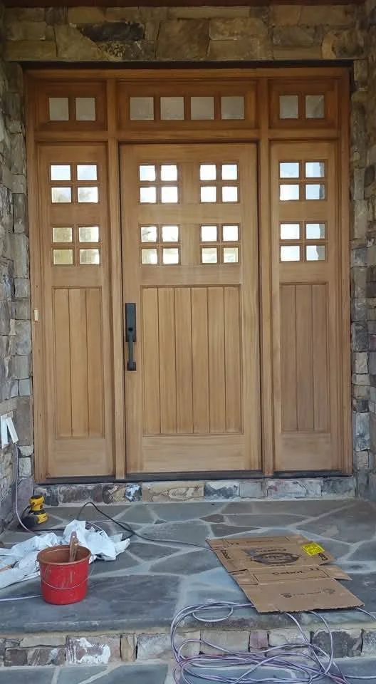 Wooden front door with small glass panes at the top, set in a stone wall.