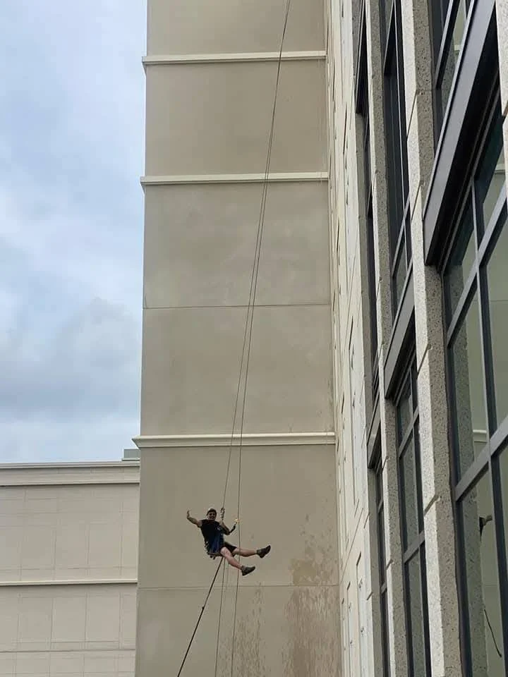 A person hanging on a rope on the side of a multi-story building during daytime.