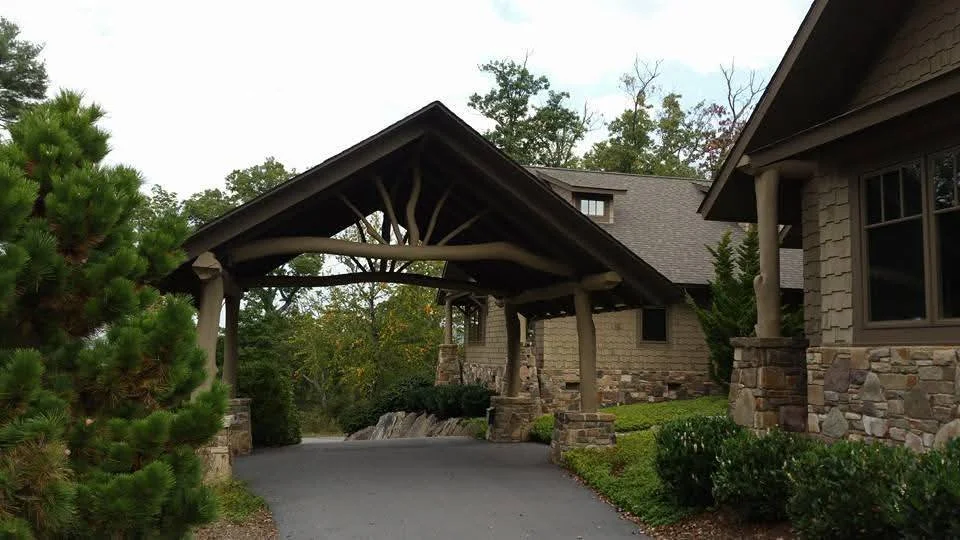 A covered driveway entrance to a house with stone exterior walls, surrounded by trees and bushes.