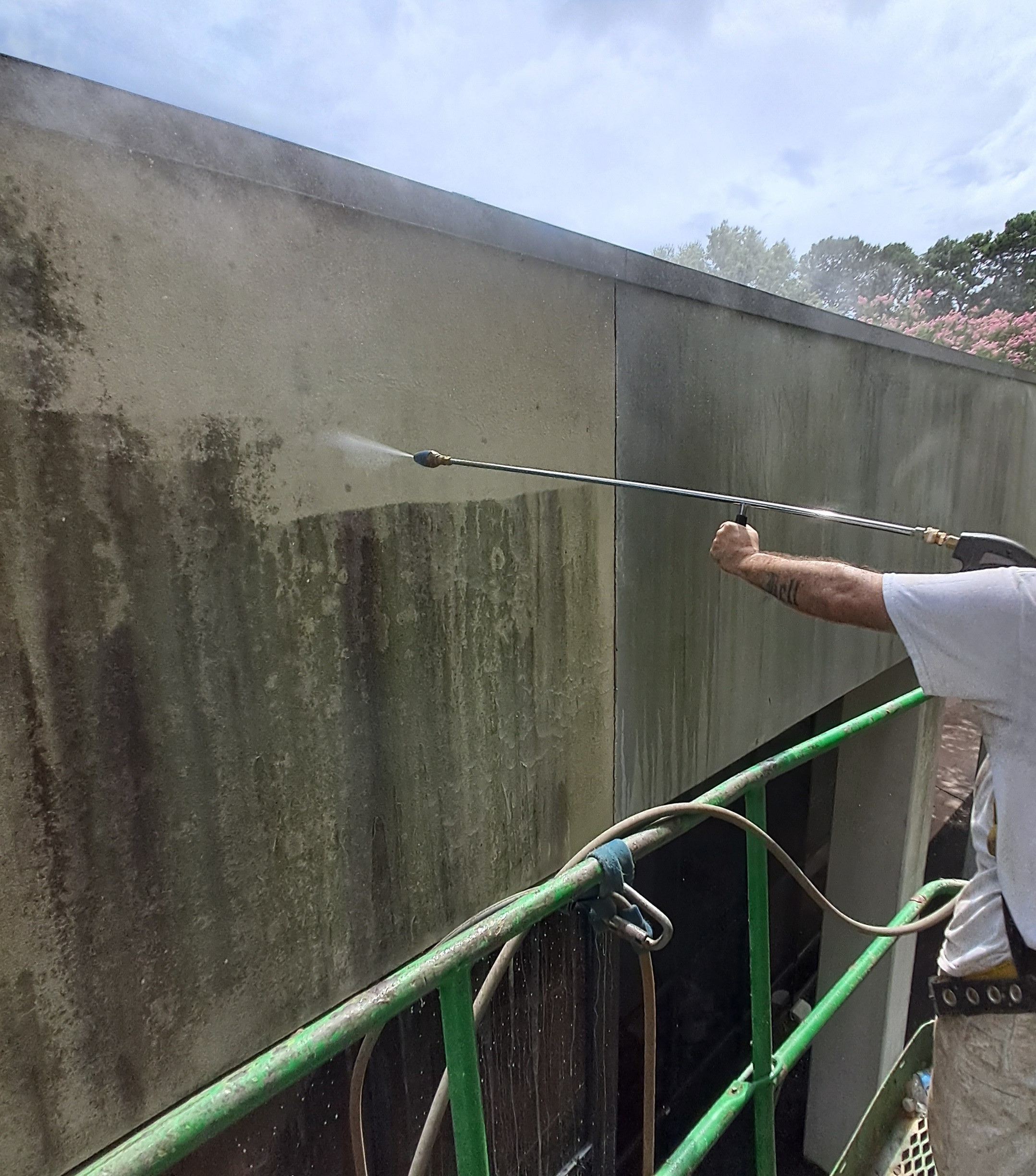 Person using a pressure washer to clean a large concrete wall outdoors.