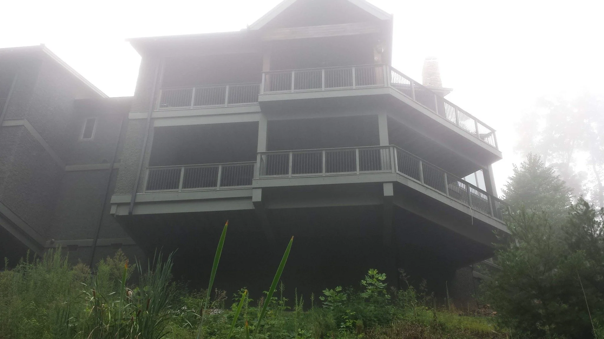 House built on stilts with multiple balconies, surrounded by fog and greenery.