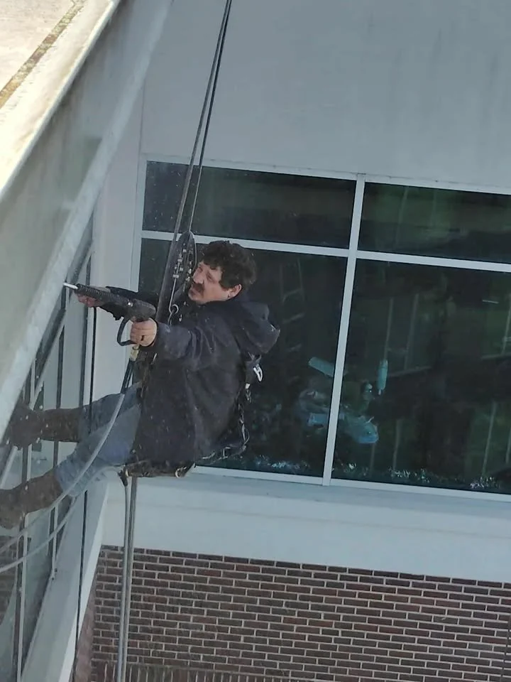A man using rope access to pressure wash outside of building.