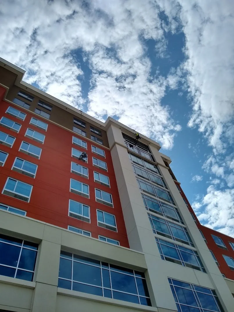 View of a multistory building with workers cleaning windows, set against a partly cloudy blue sky.
