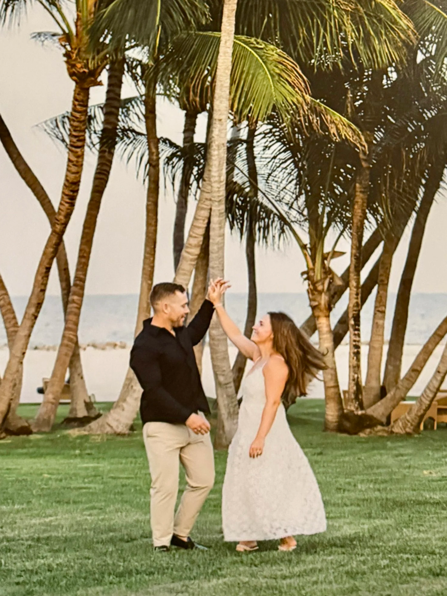 A newly wed couple dancing outdoors on a grassy area with palm trees and a beach in the background. at the Islander Resort, Islamorada Florida, in the Florida Keys.