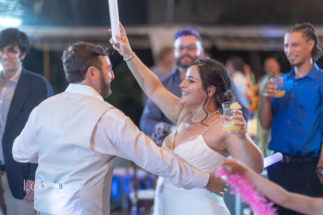 A woman in a white dress and a pearl necklace holding a drink with lemon slices, smiling as she dances with her husband at a wedding reception where a Steel Drum player played the cocktail hour live music. Hemingway House and Museum, Key West Florida
