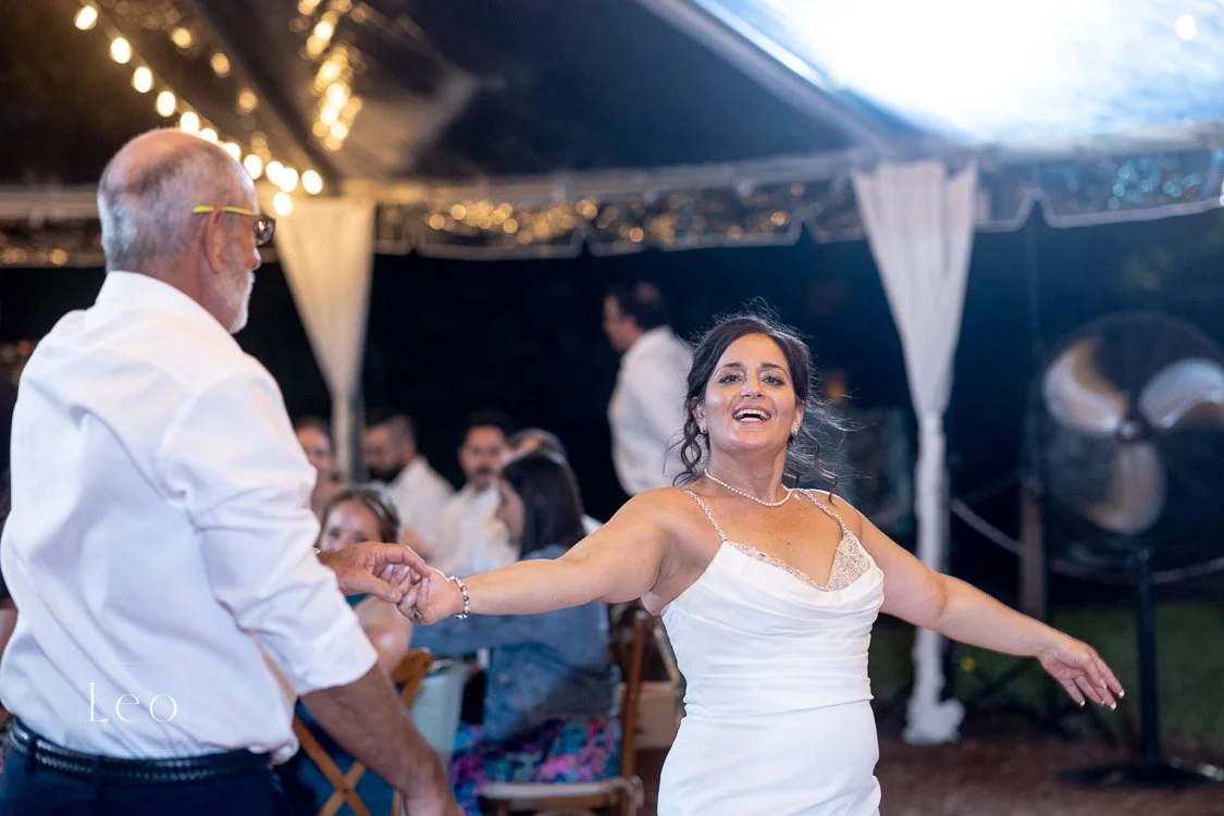 A woman in a white dress dancing with a man in a white shirt at a wedding reception celebration under a tent with guests and string lights. Hemingway House and Museum, Key West Florida