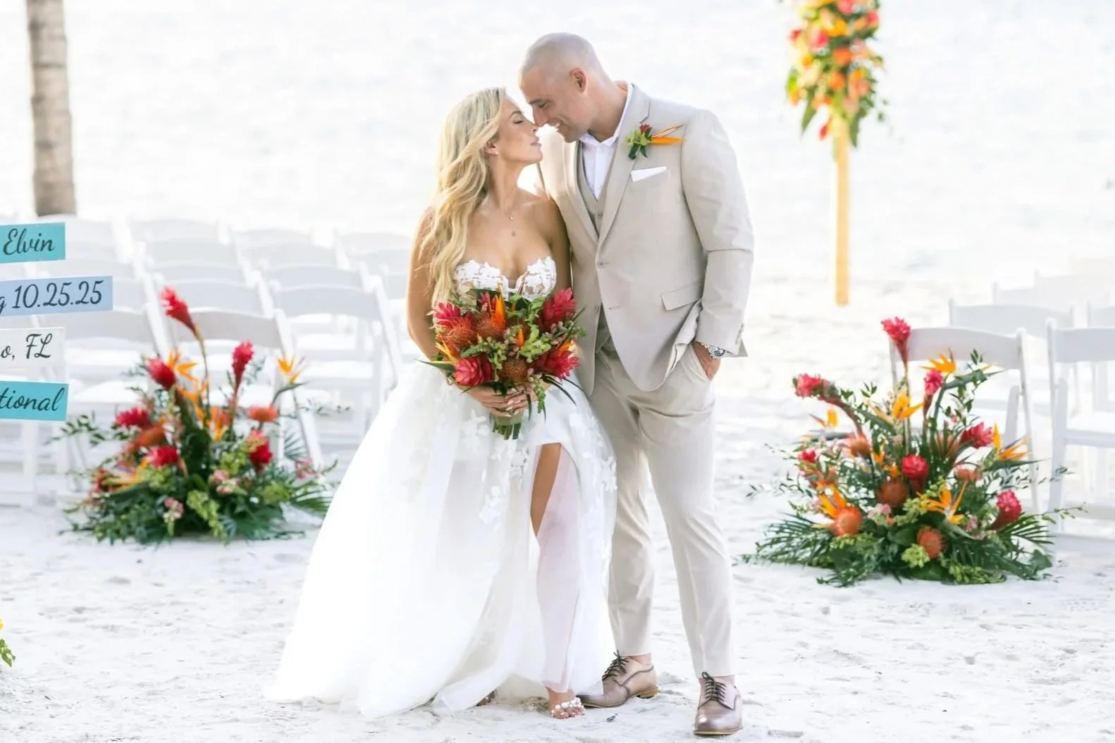 A bride and groom standing close at their beach wedding ceremony, where steel drum music is playing, with the bride holding a colorful bouquet and the groom wearing a light-colored suit under a clear sky. Playalargo, Key Largo, Florida, Florida Keys