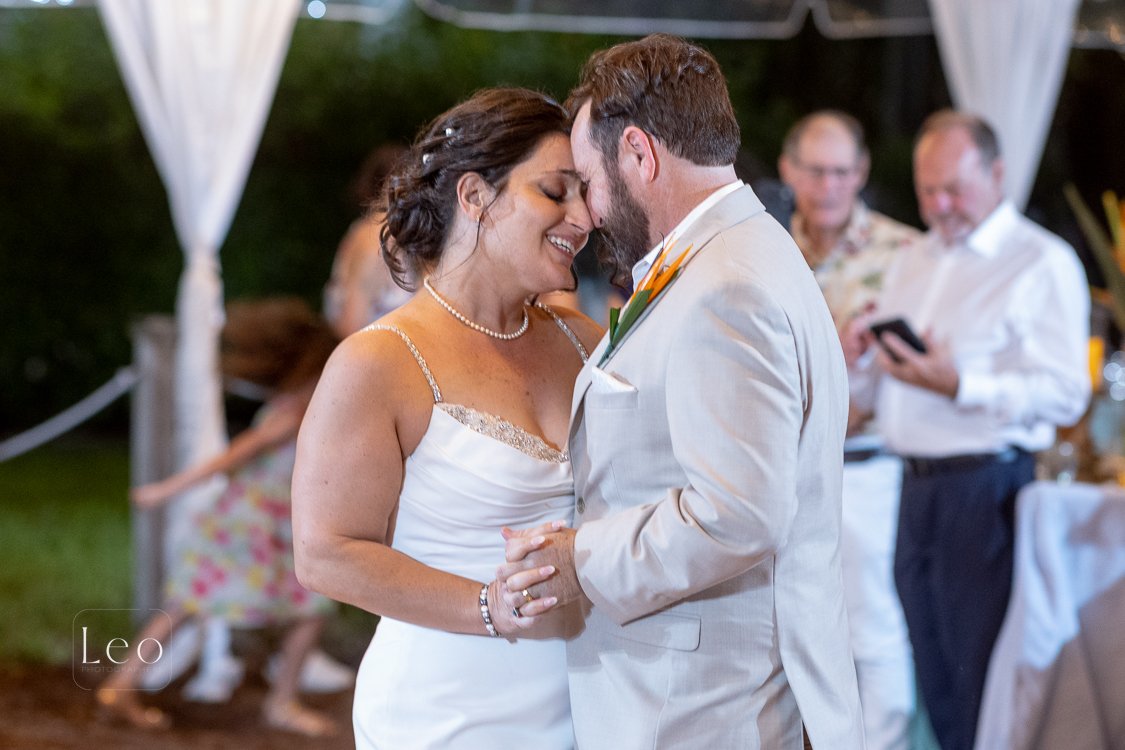 A bride and groom dancing closely at their wedding reception, smiling with foreheads touching, with guests in the background. Hemingway House and Museum, Key West Florida