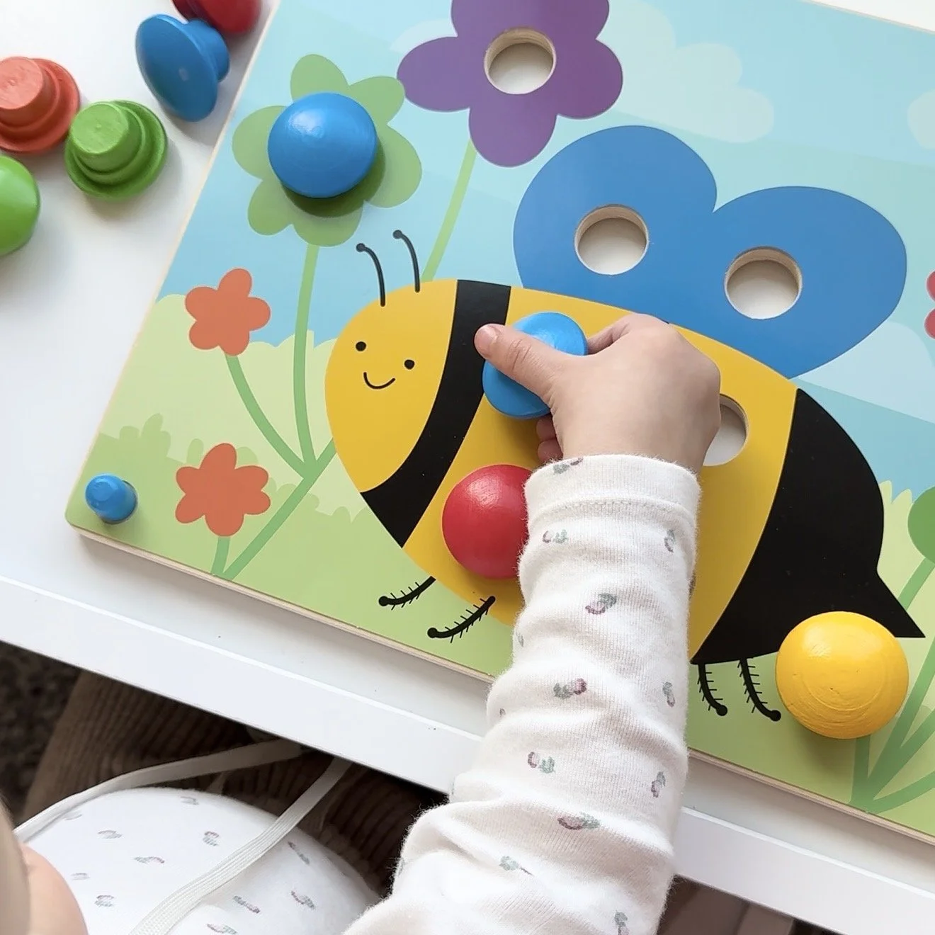 Child playing with a wooden toy with flowers and bees, placing a button on an open slot.