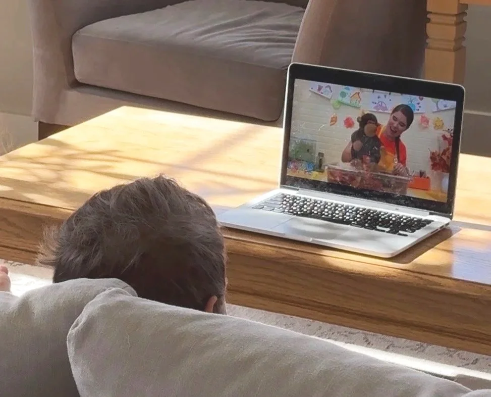 Child lying on a sofa watching a low-stimulating show of a teacher singing.