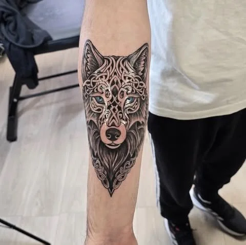 Tattoo of a wolf's face with intricate tribal-style details on a person's forearm.
