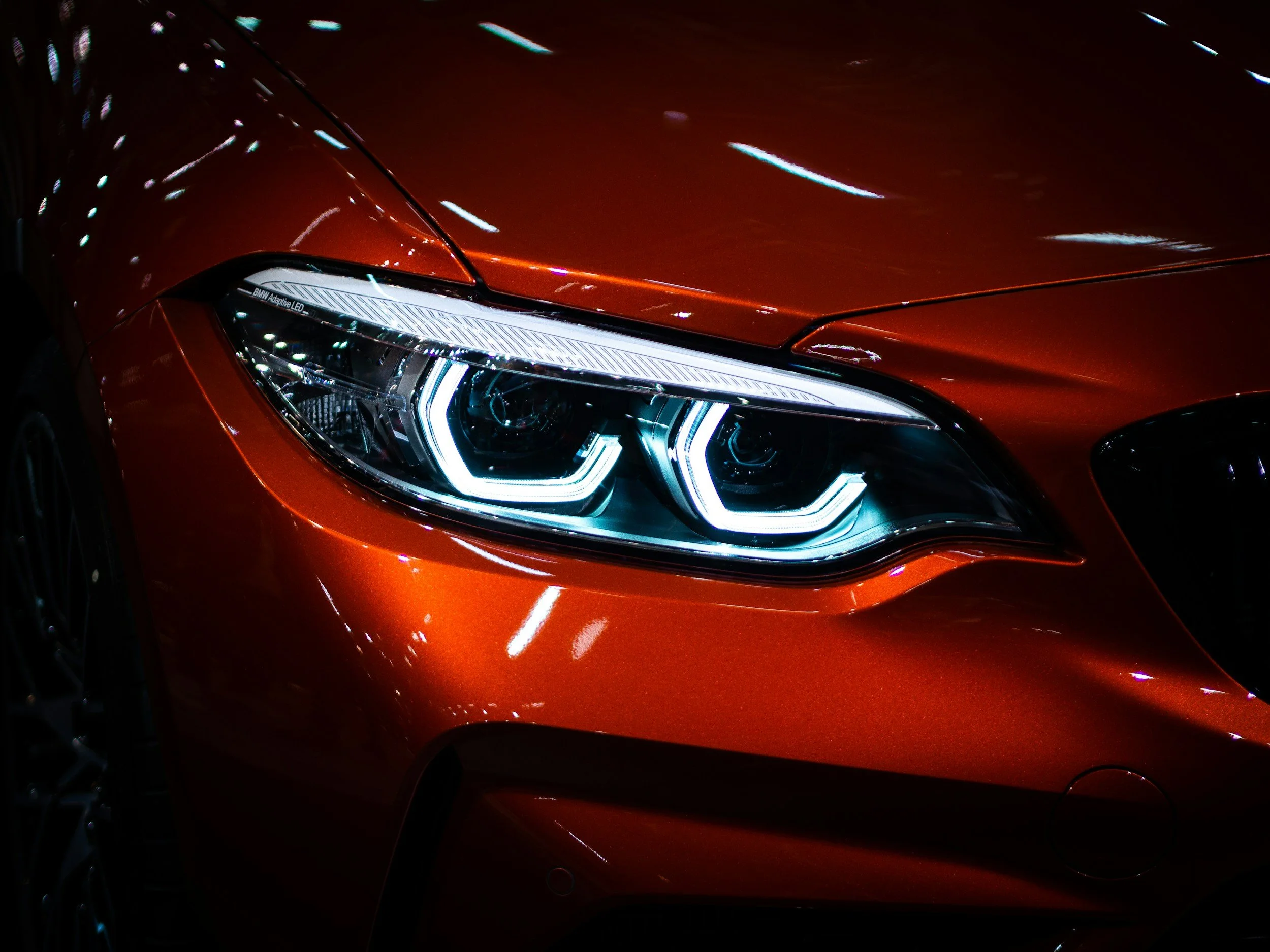 Close-up of an orange car's headlight with bright LED lights and reflections on its sleek, shiny surface.