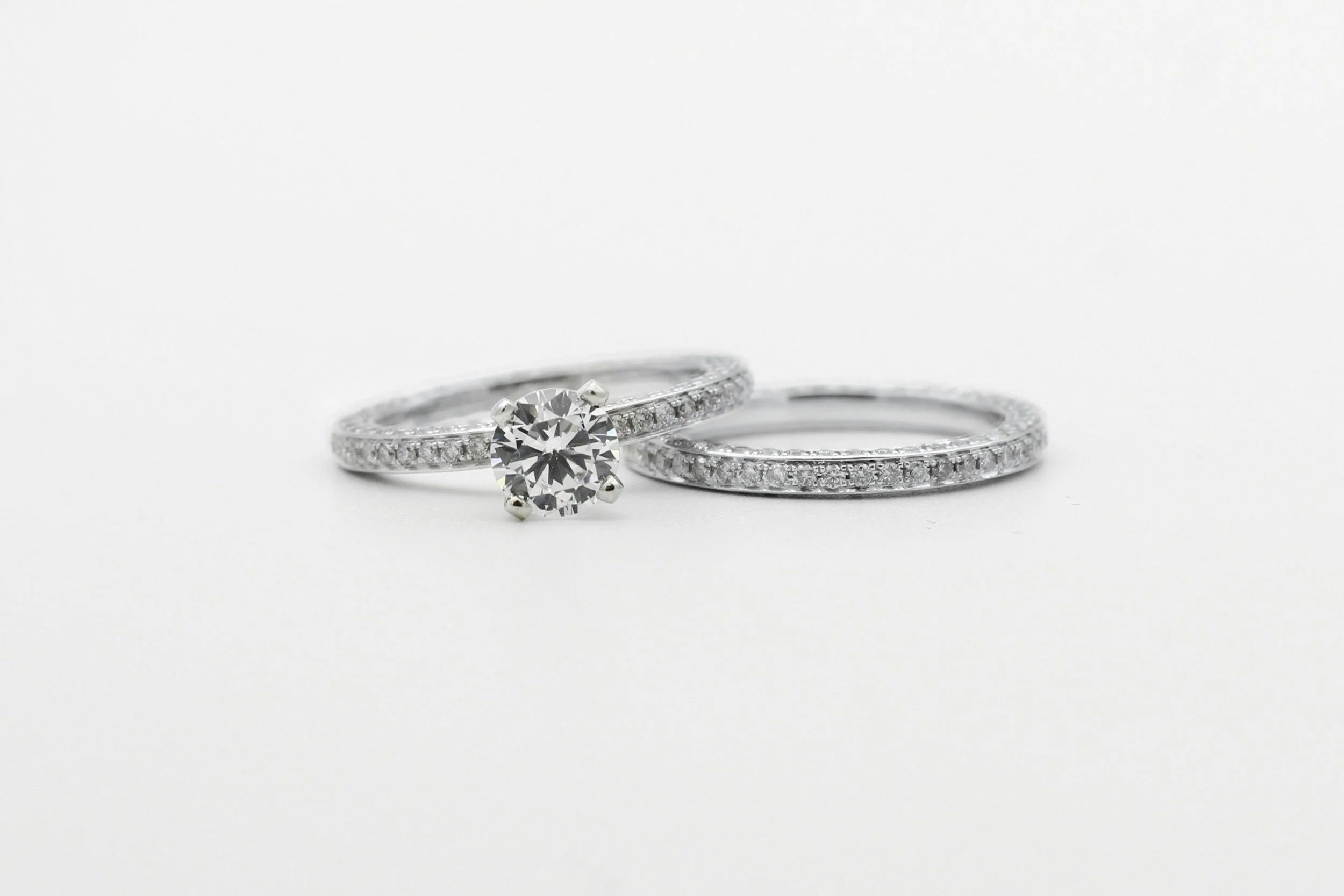 Close-up of a diamond engagement ring with a large central diamond and a wedding band set with smaller diamonds, both placed on a white background.