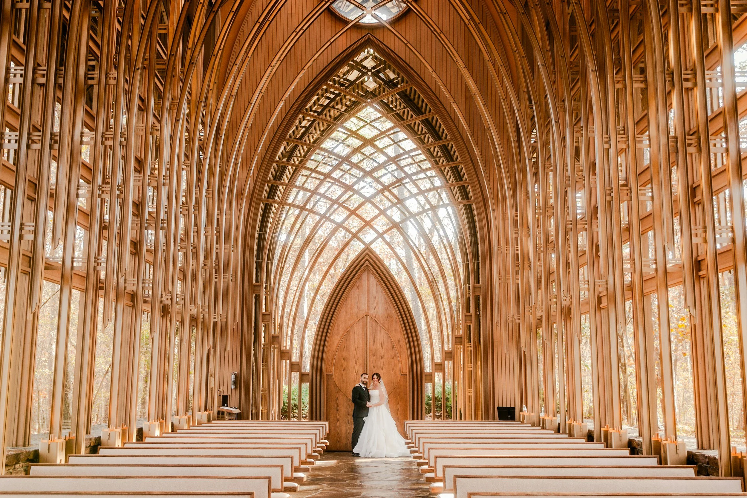 A bride and groom standing together inside a wooden church during a wedding ceremony. The church has high vaulted ceilings with intricate wooden arches and large windows, allowing natural light to fill the space.