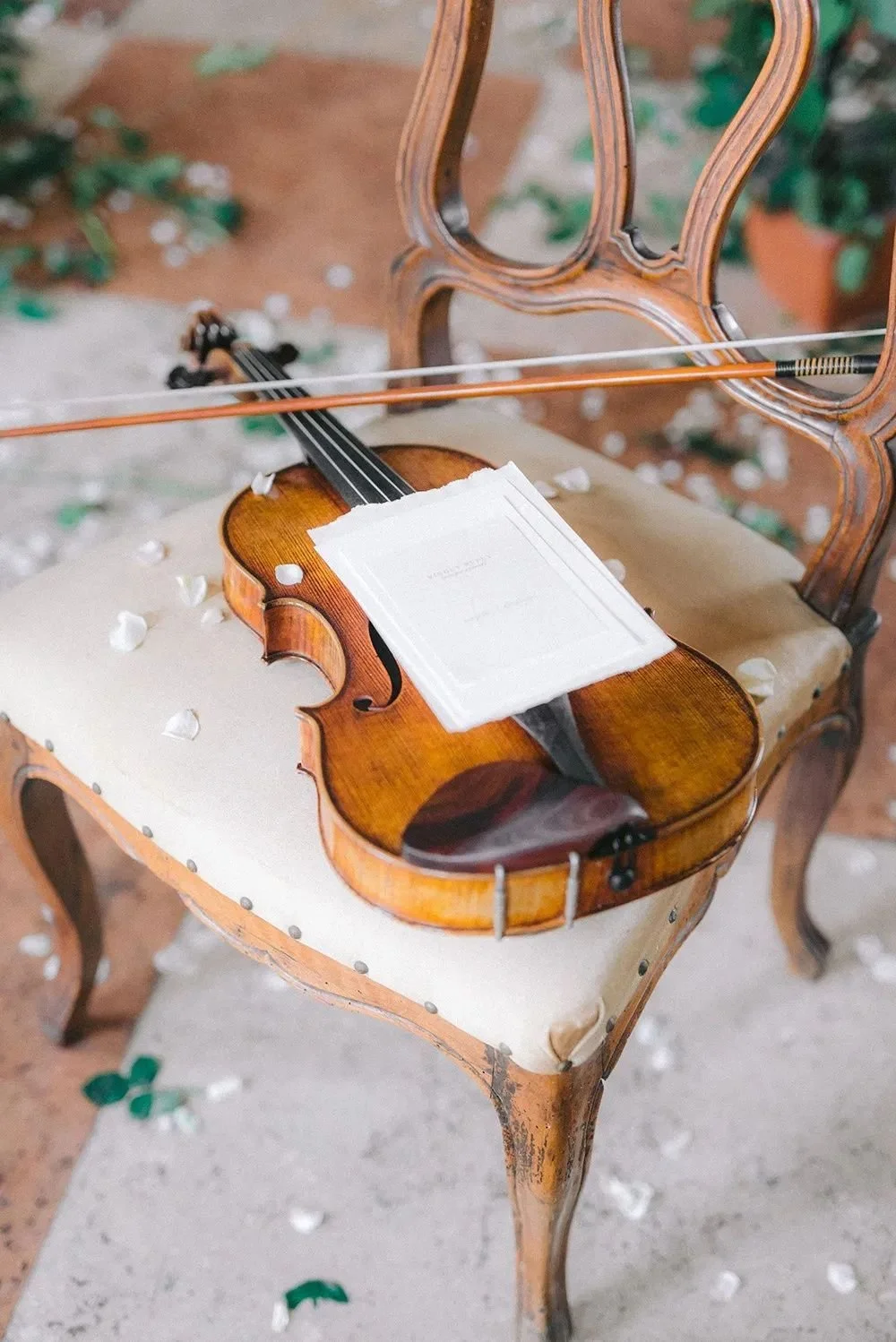 Violin resting on an antique chair surrounded by petals, representing romantic live violin music for wedding ceremonies.