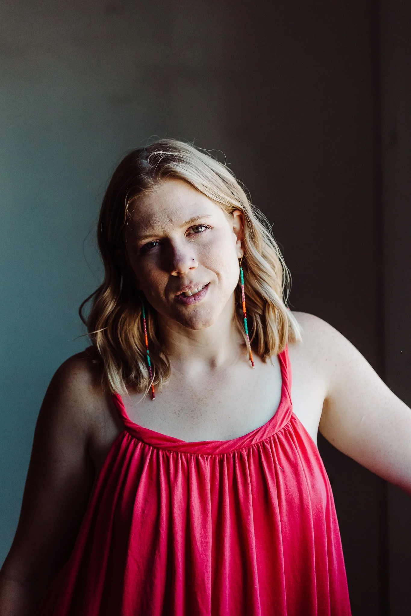 A woman with shoulder-length blonde hair, wearing a red sleeveless dress and colorful beaded earrings, standing indoors near a window | Amy Wilder Studio - Brand Strategist + Web Design