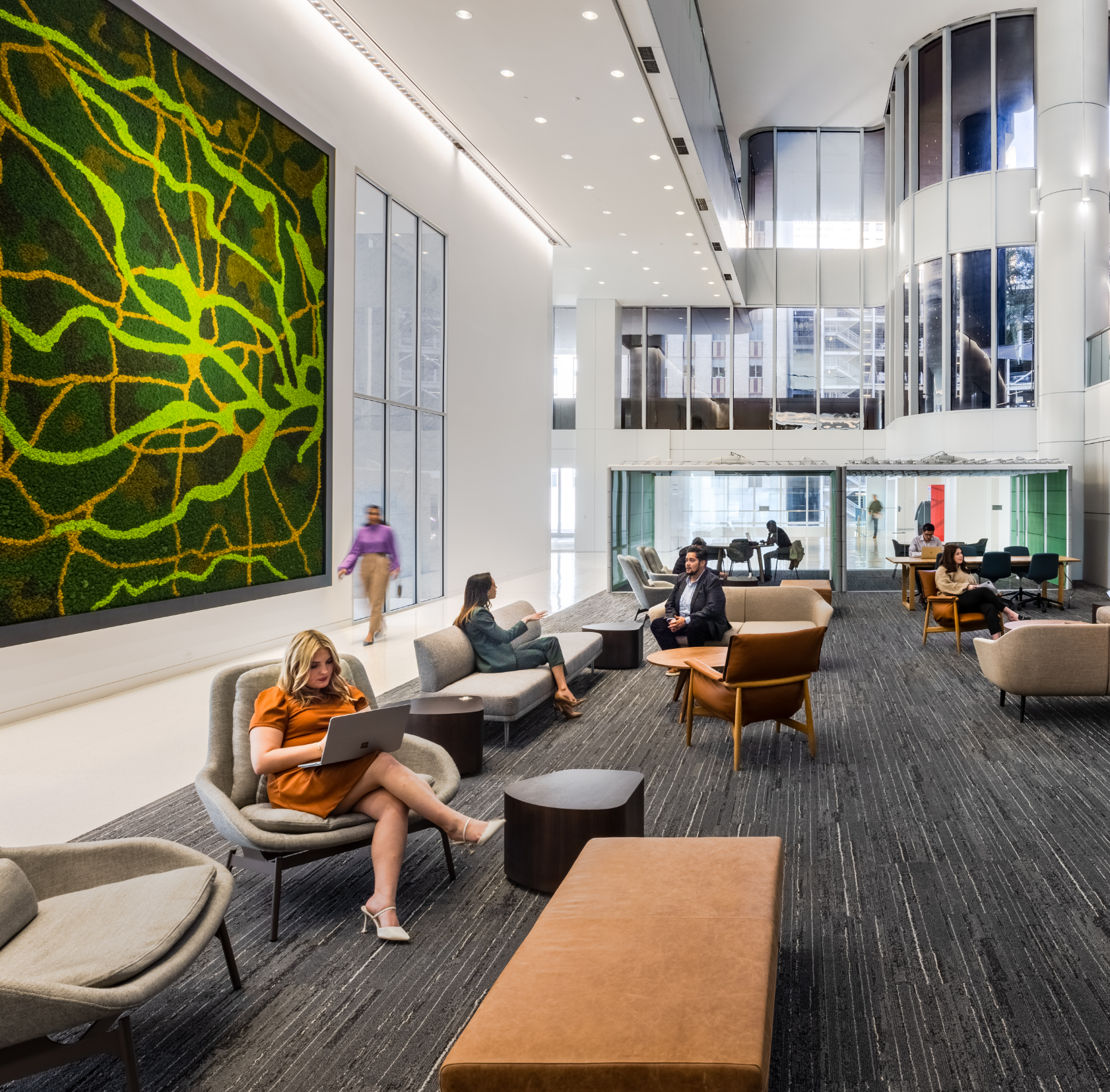 Modern office lobby with seating area, large green abstract wall art, glass walls, and people working or relaxing.