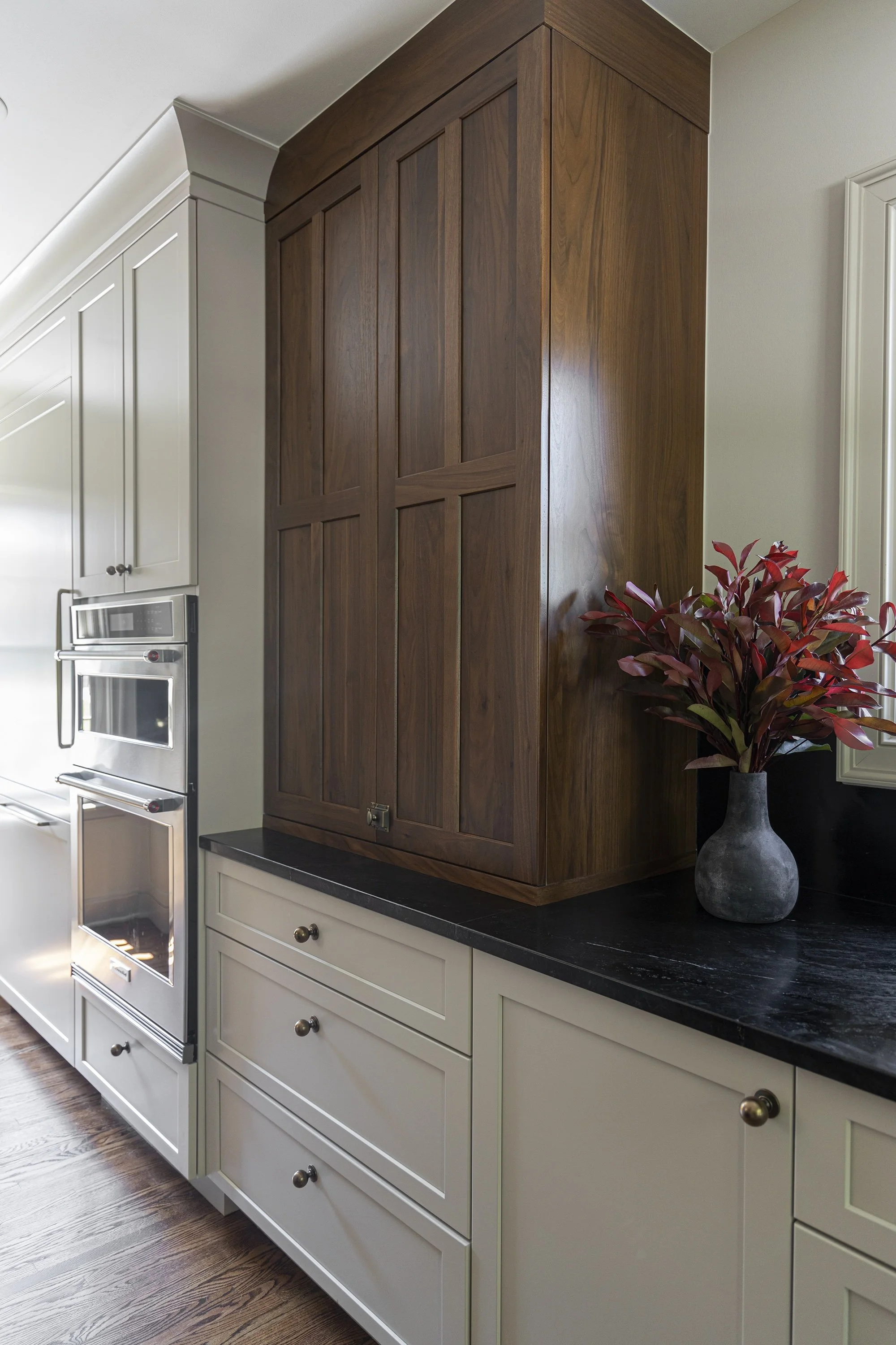 Kitchen with white cabinets, a black countertop, a dark wooden wall cabinet, a potted plant with red leaves, and a built-in oven.
