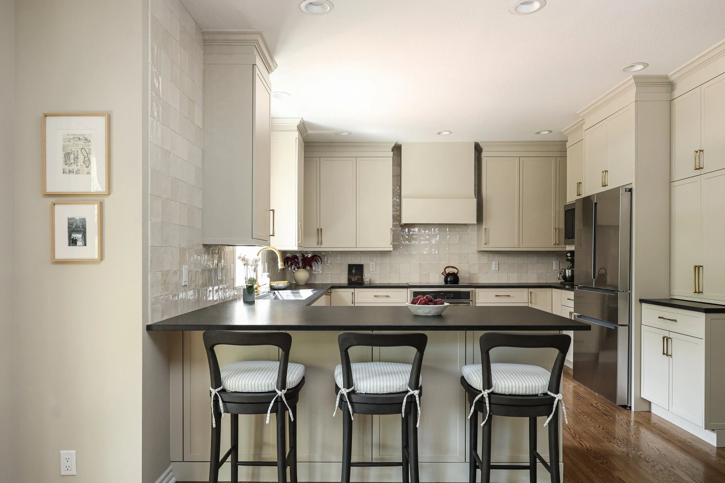 Modern kitchen with white cabinets, black countertops, stainless steel appliances, and a kitchen island with three black chairs with striped cushions.