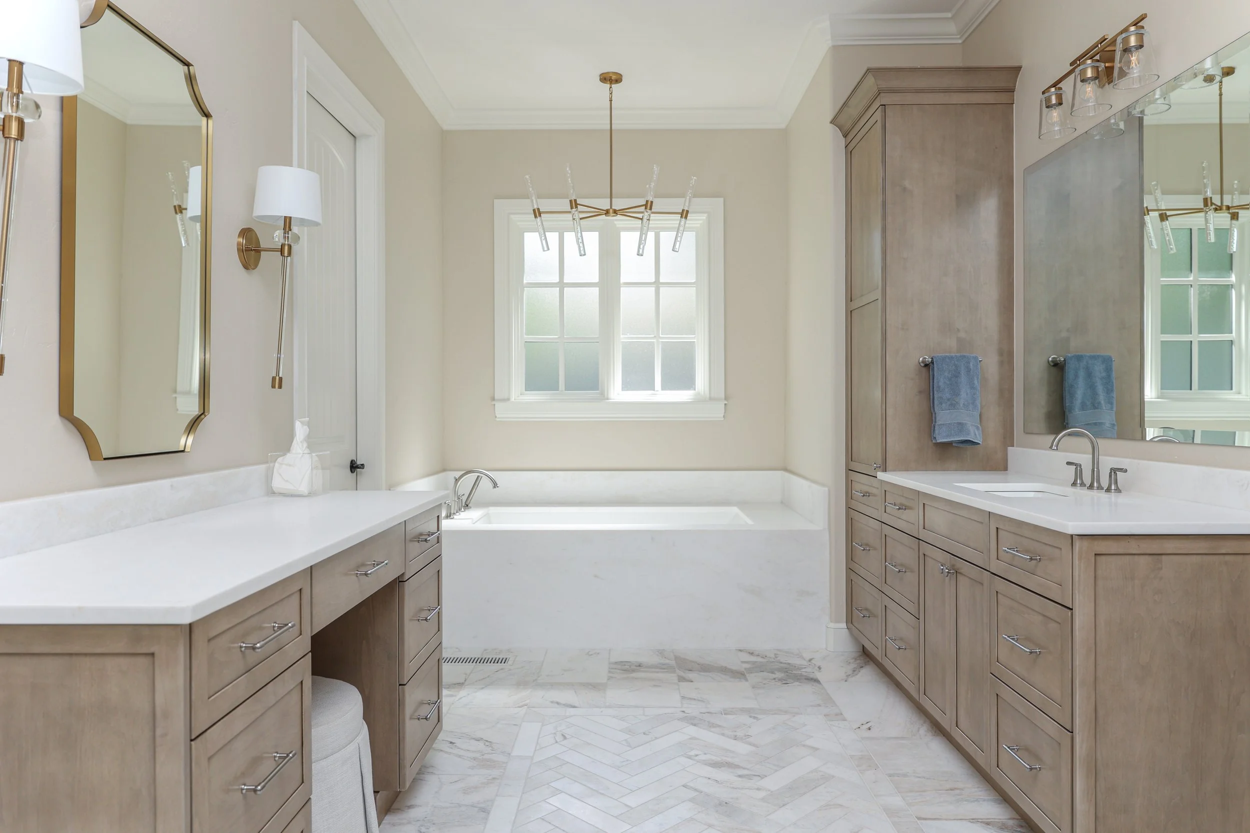 Bright bathroom with vanity, large mirror, wall-mounted lights, bathtub, window, and neutral tones.