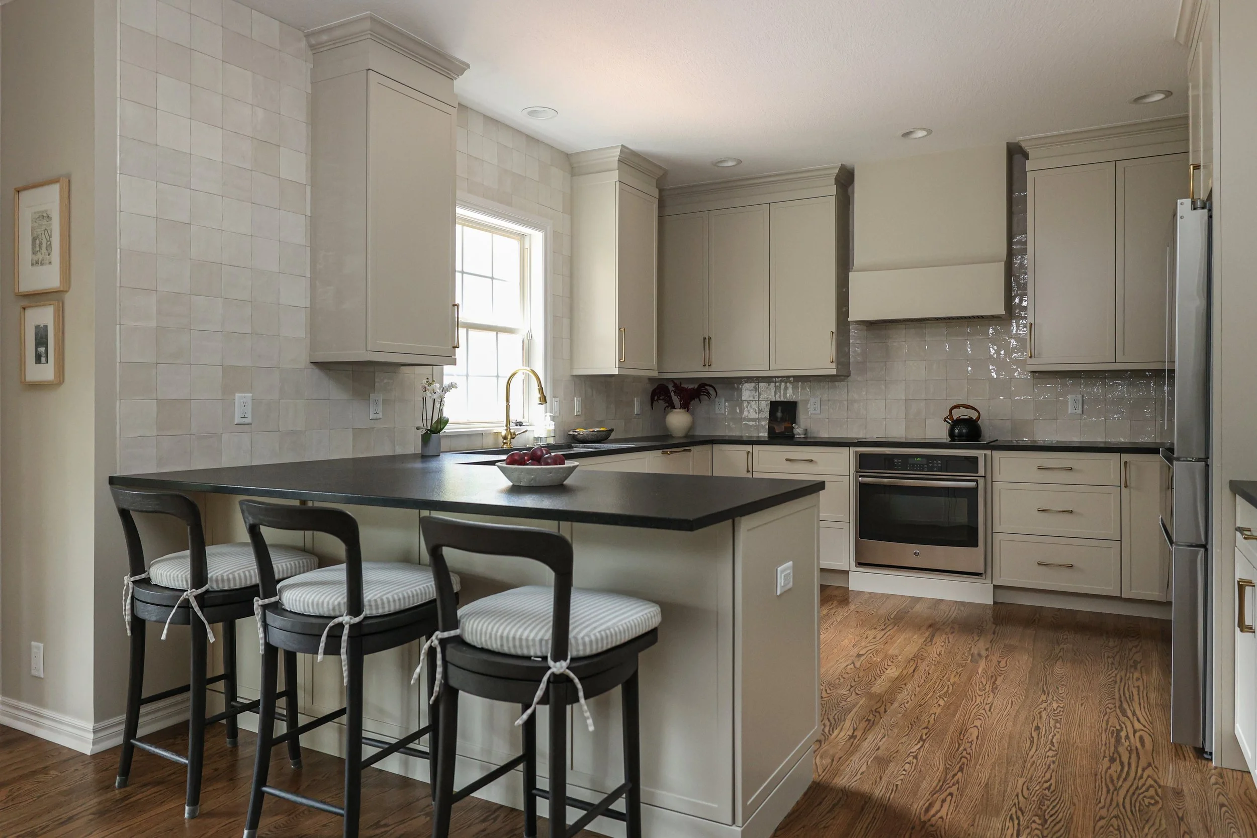 Modern kitchen with beige cabinets, black countertop, wooden floors, and a central island with three chairs.