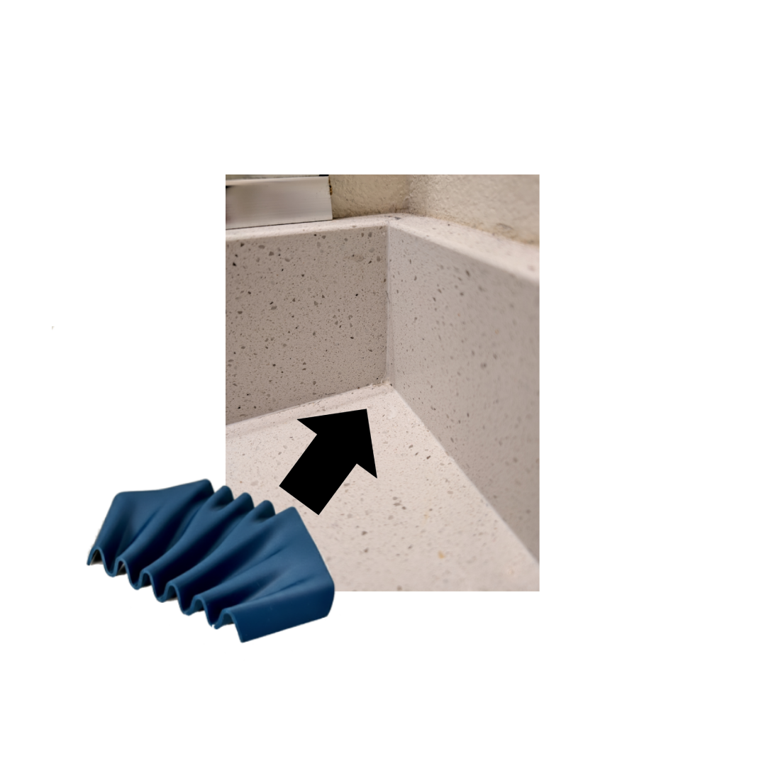 Close-up of a corner of a kitchen countertop with a metal trim, with a black arrow pointing to the edge of the counter and a blue accordion-style tube or cover at the bottom left.