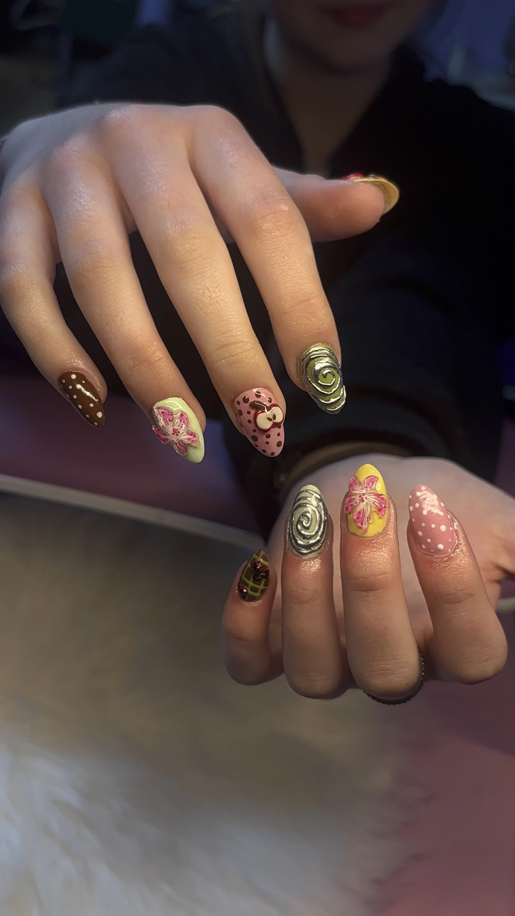 Close-up of two hands with intricate, colorful nail art featuring floral, swirl, and polka dot designs.