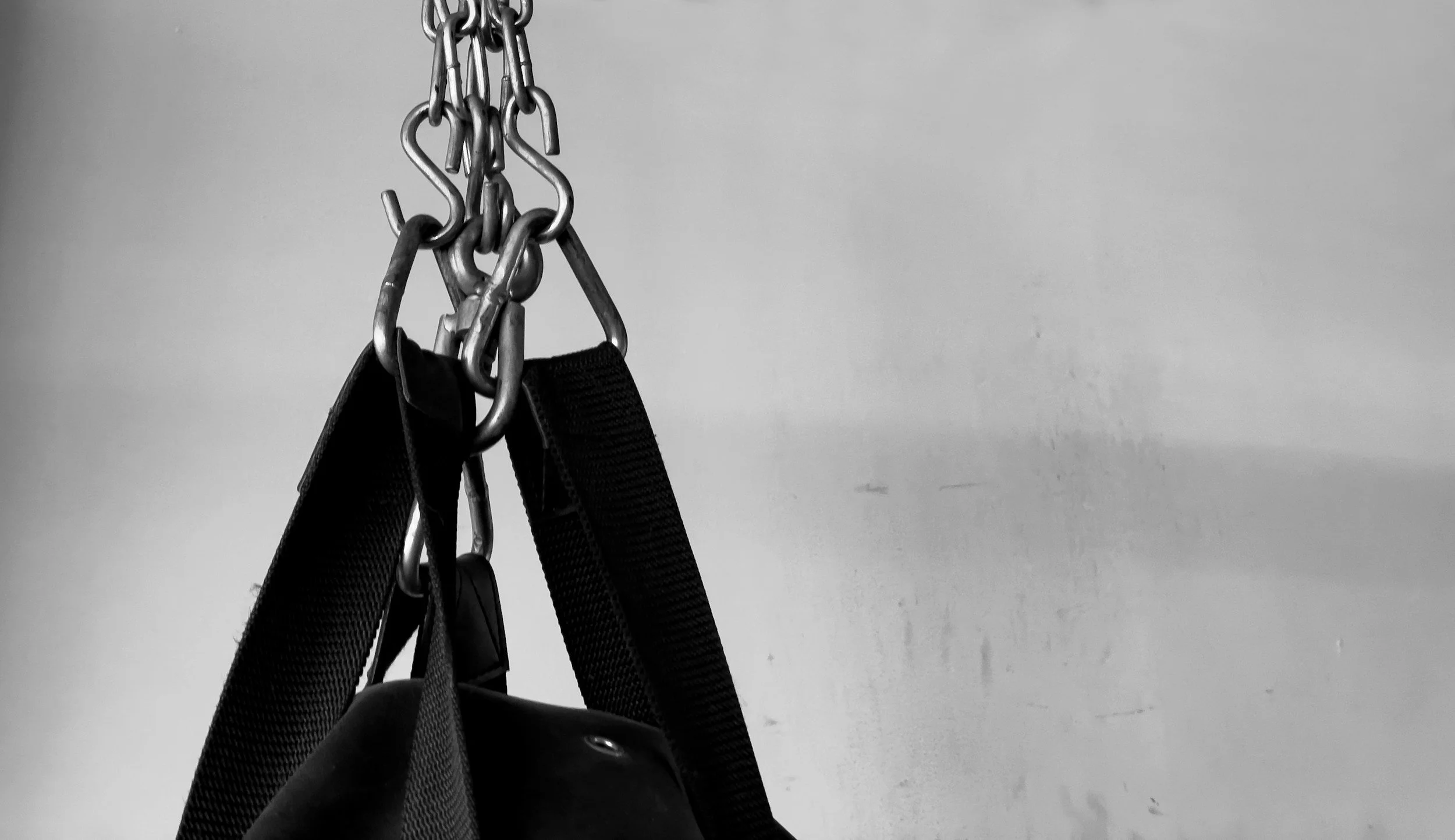 Black leather bag hanging from a metal chain with hooks, attached to a wall.