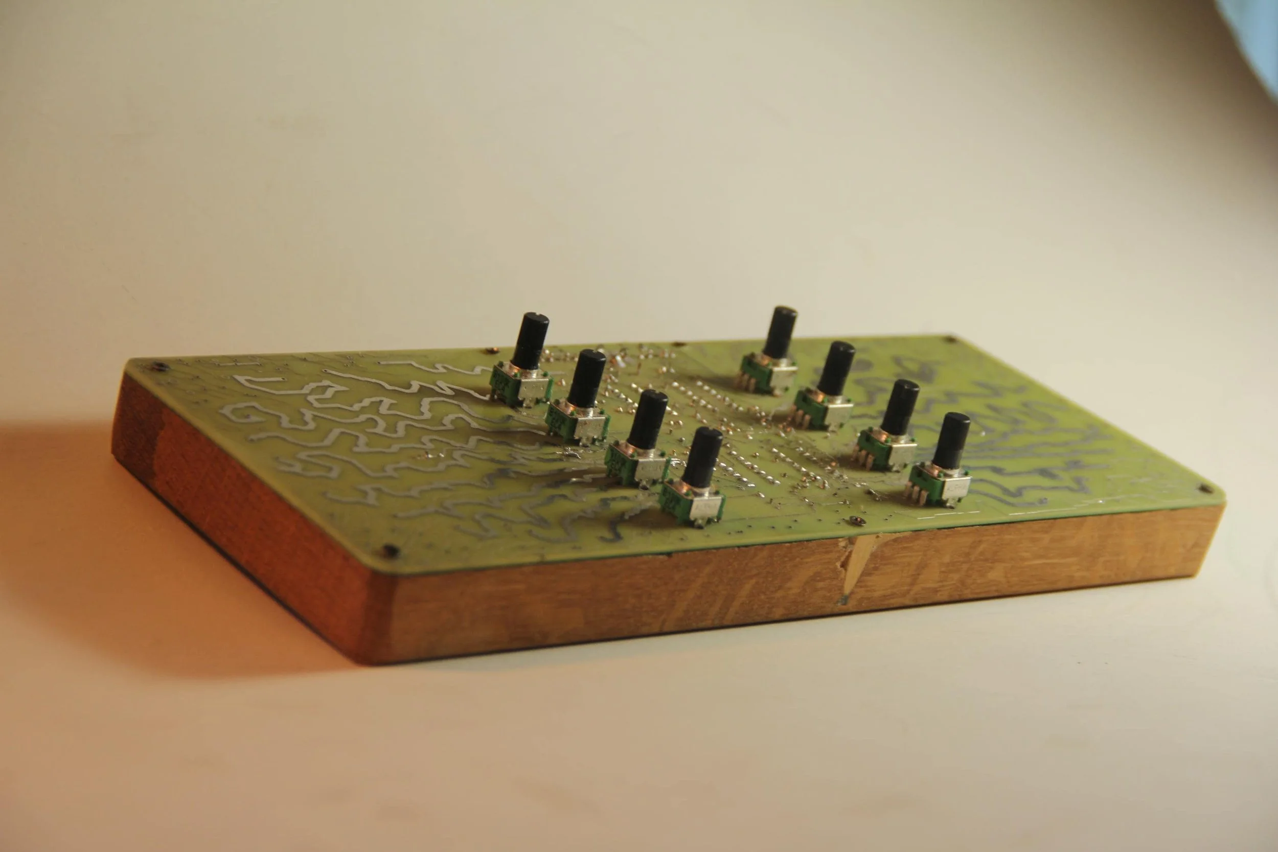 A vintage circuit board with black switches mounted on it, resting on a wooden base.