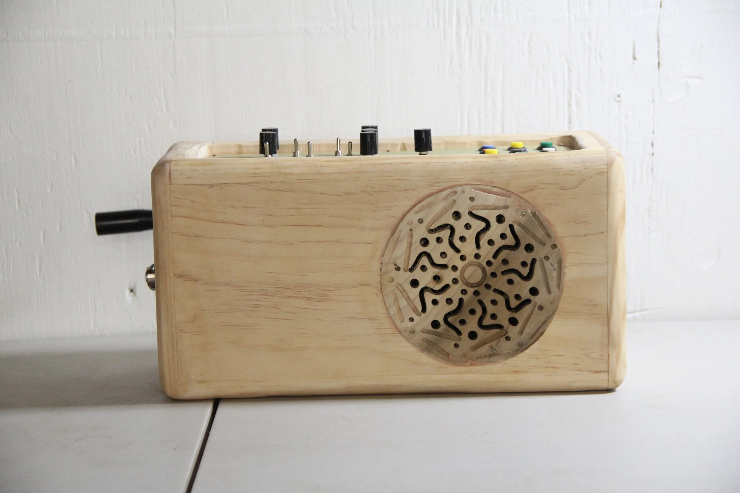 A wooden electronic instrument with knobs and switches, featuring a circular metal grille on the front.