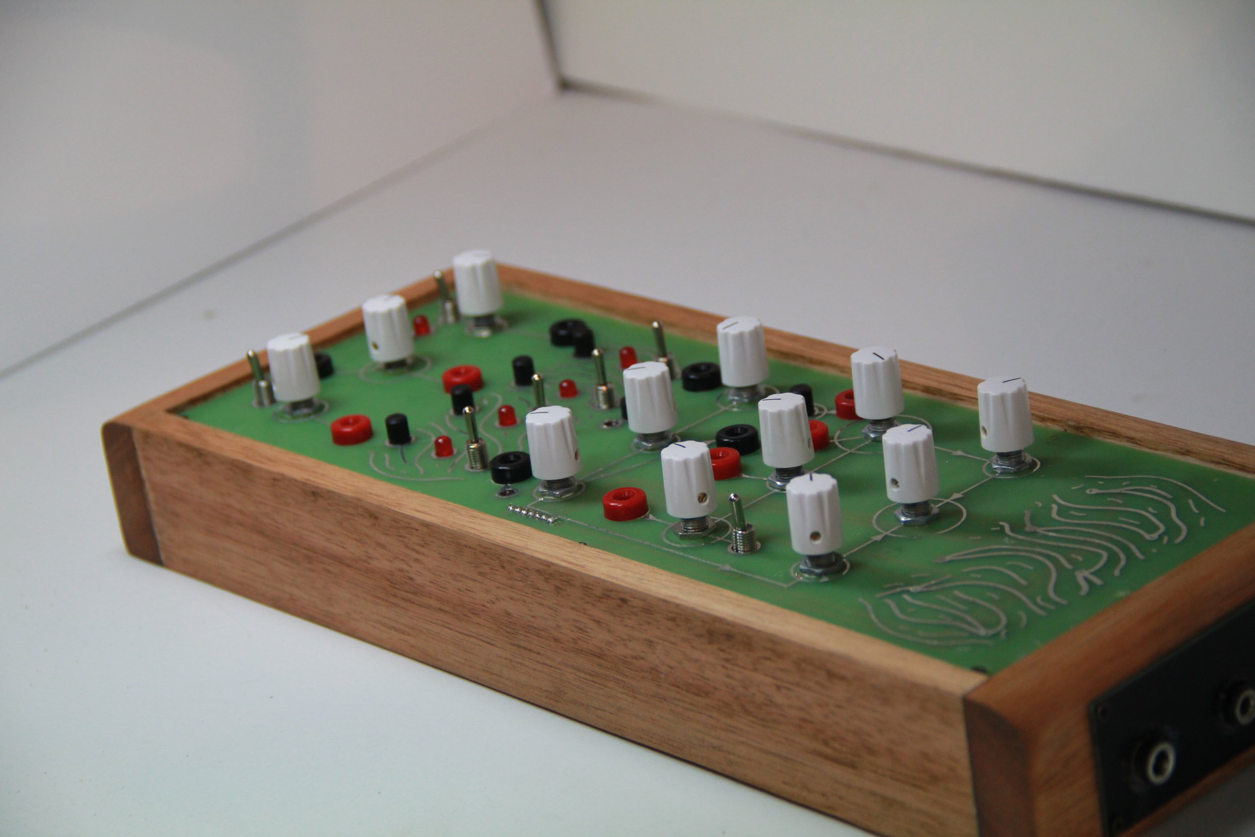 A vintage mechanical board game with a wooden frame, white knobs, and red and black game pieces on a green circuit-like playing surface.