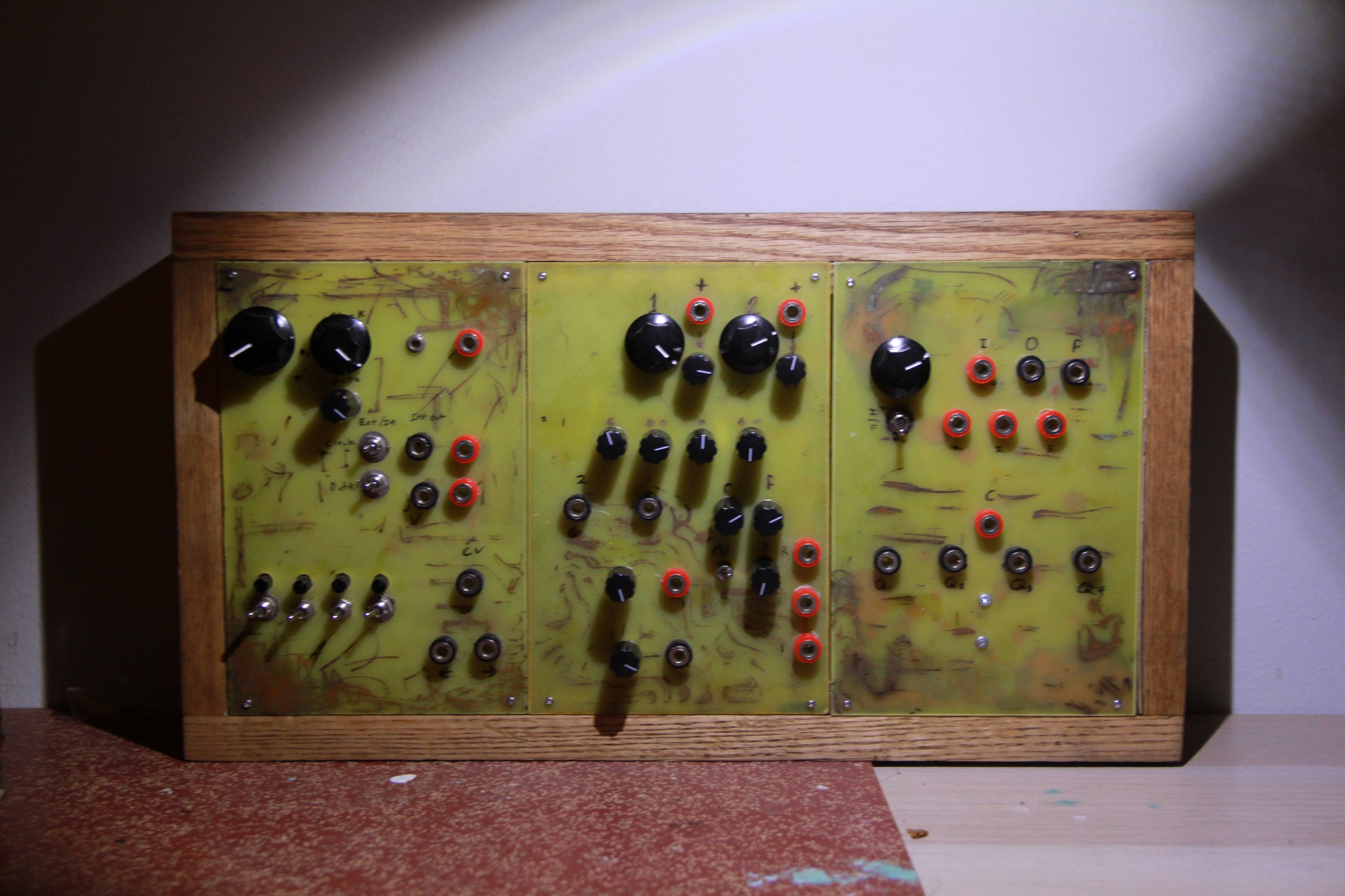 A vintage synthesizer with black knobs, red jacks, and metal switches mounted in a wooden frame.