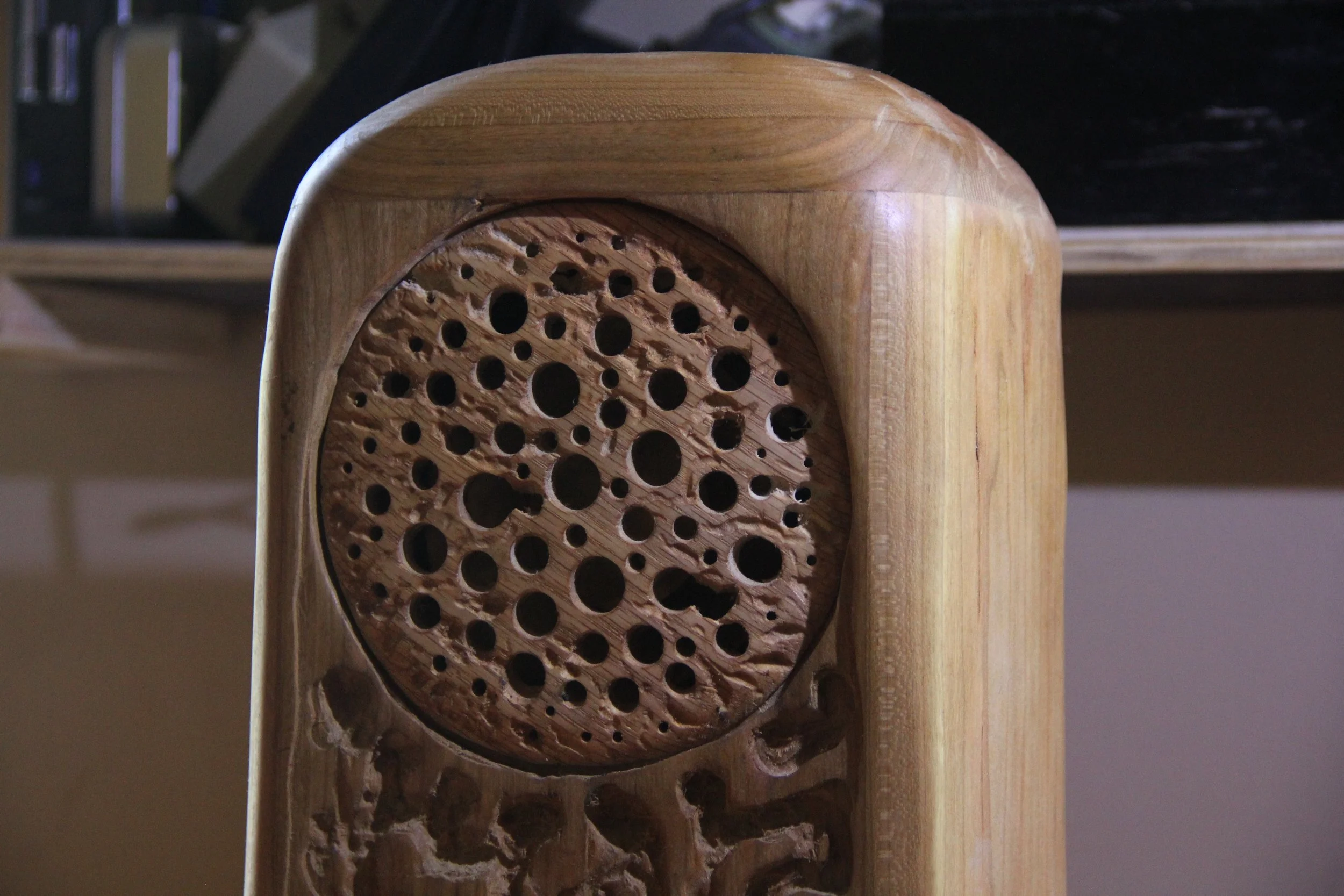 Close-up of a wooden object with a circular, intricate carved pattern of various-sized holes, part of a furniture or decorative piece.