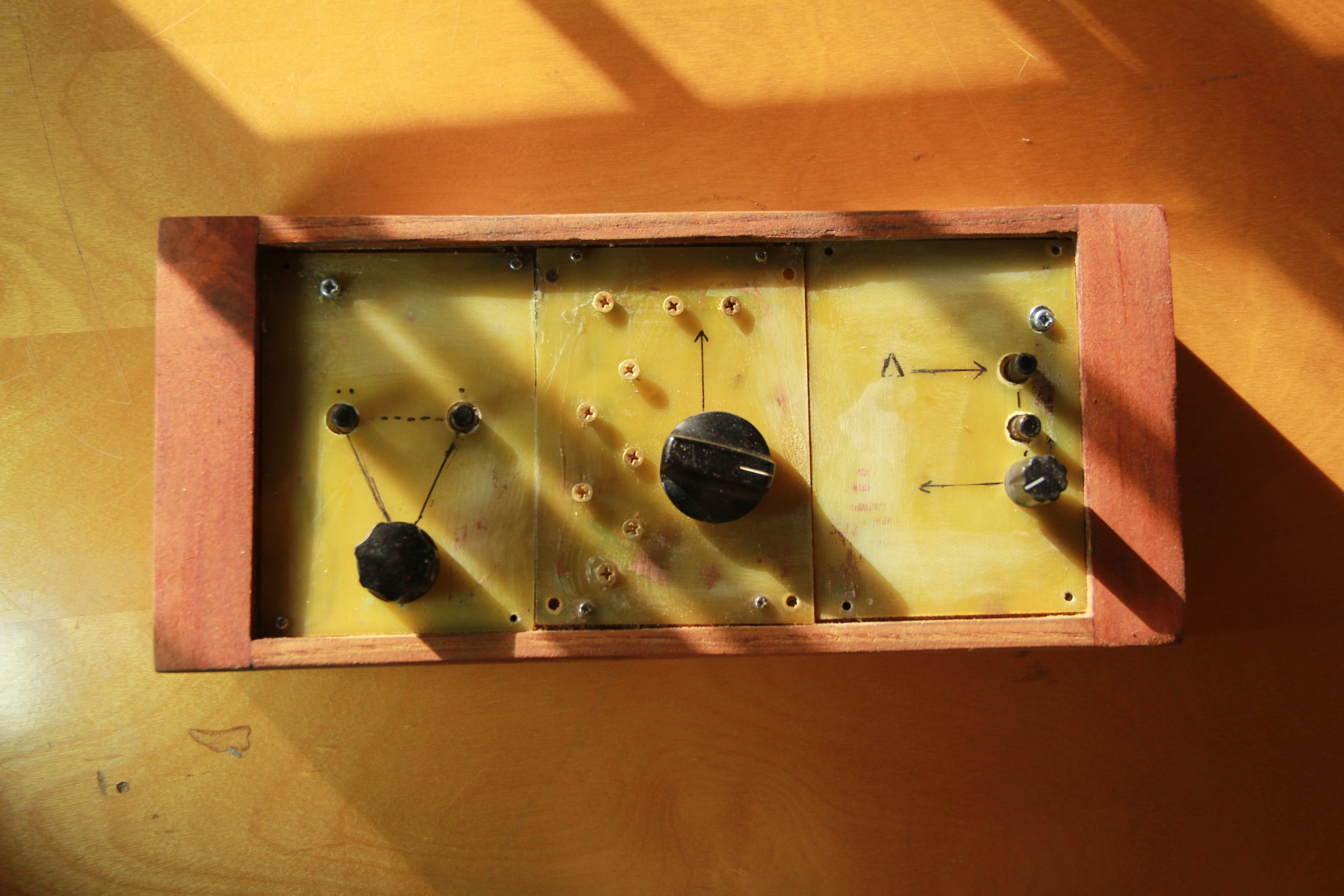 A vintage wooden and metal box with knobs, screws, and hand-drawn arrows, resembling an electronic or experimental device.