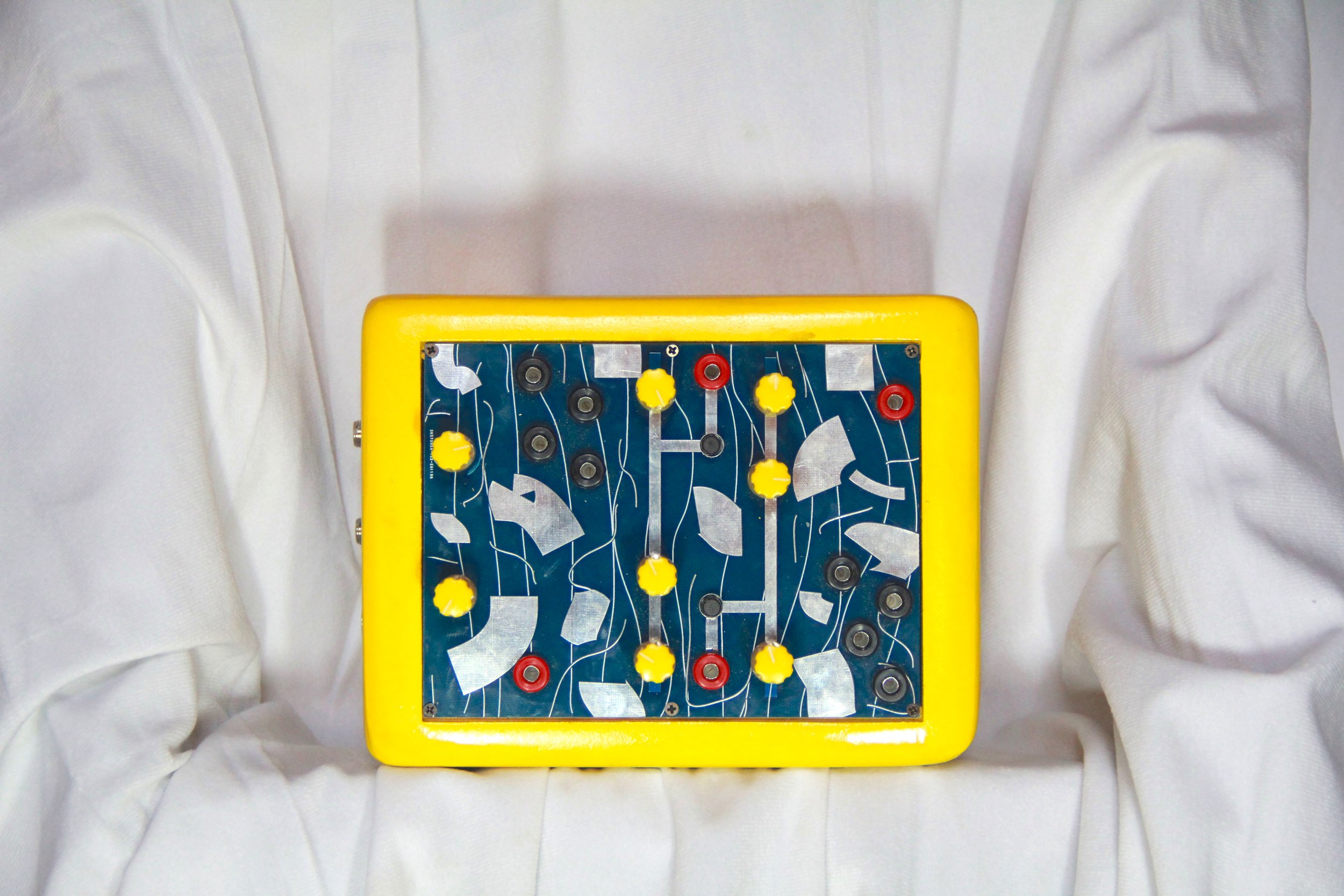 A vintage game board with yellow knobs and a dark blue background, featuring metal and plastic components, on a white cloth backdrop.