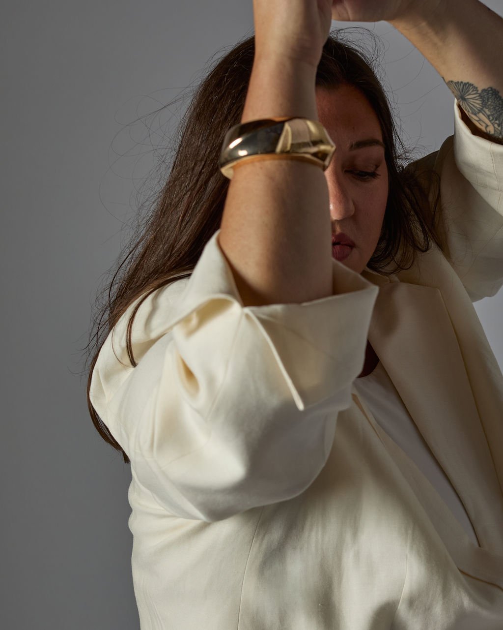 Tanya Jacobson, Capacity advisor that removes founder dependency and expands capacity for scaling founders, wearing a cream-colored blazer and a gold bracelet, is posing with her eyes closed against a plain background.