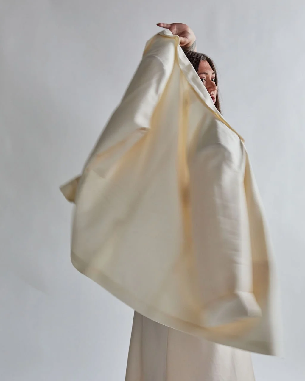 Tanya Jacobson, Capacity advisor that removes founder dependency and expands capacity for scaling founders, holding a large beige satin or silk fabric curtain or drape, with a plain white background.
