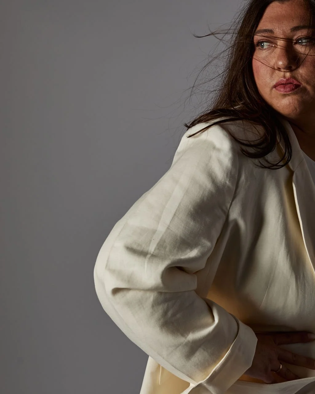 Tanya Jacobson, Capacity advisor that removes founder dependency and expands capacity for scaling founders, wearing a cream-colored blazer, looking to the right with her hand on her hip, against a gray background.