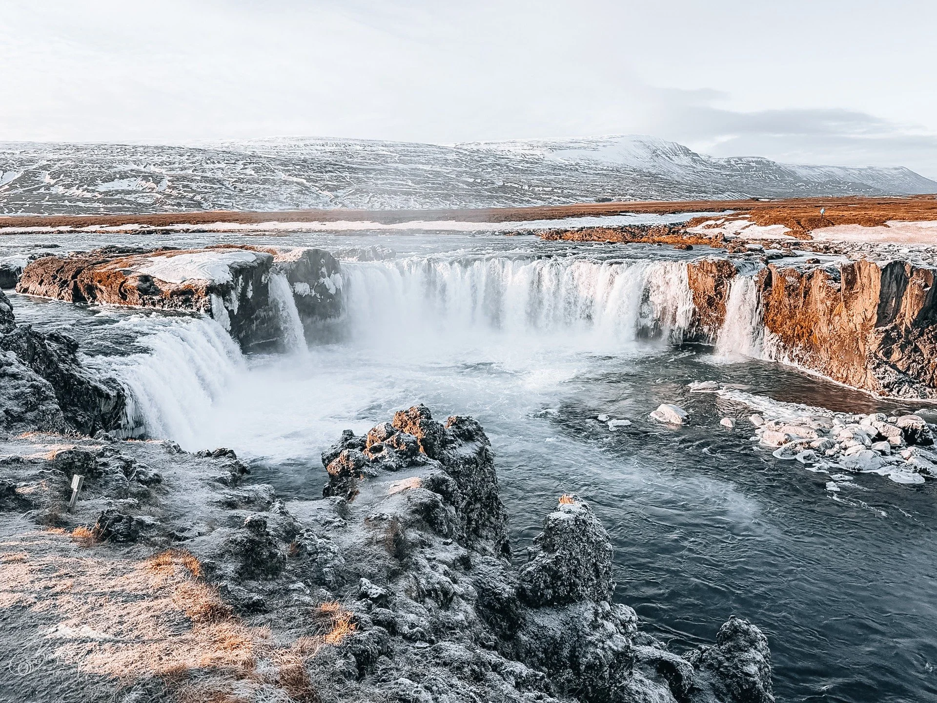 At Selfoss, the J&ouml;kuls&aacute; &aacute; Fj&ouml;llum fans outward, spilling gently over a wide basalt rim before narrowing and accelerating toward Dettifoss downstream. The water moves with intention rather than violence, curling over the edge i