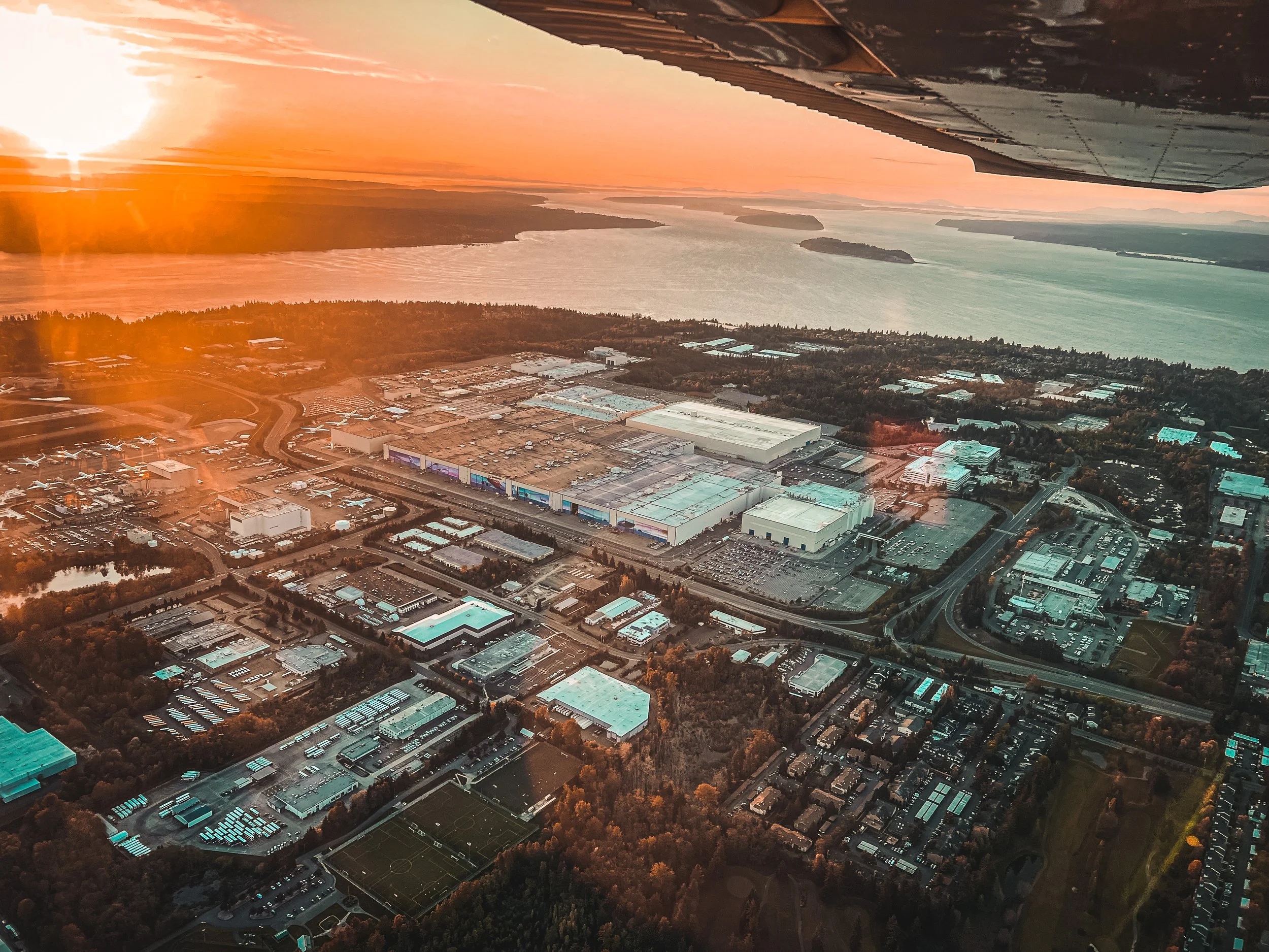 Aerial view of Boeing near the Puget Sound during sunset, with the airplane wing visible at the top of the image.
