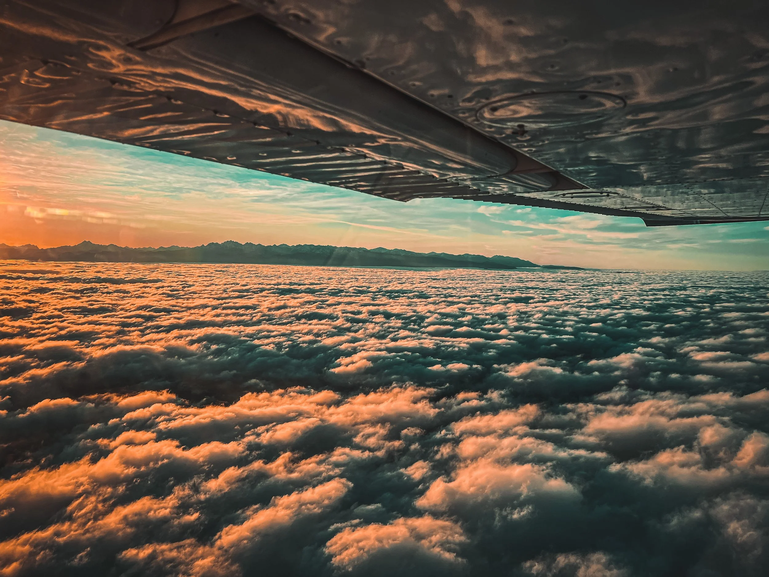 View from an airplane window showing clouds during sunset with the Olympic Mountain Range in the distance.