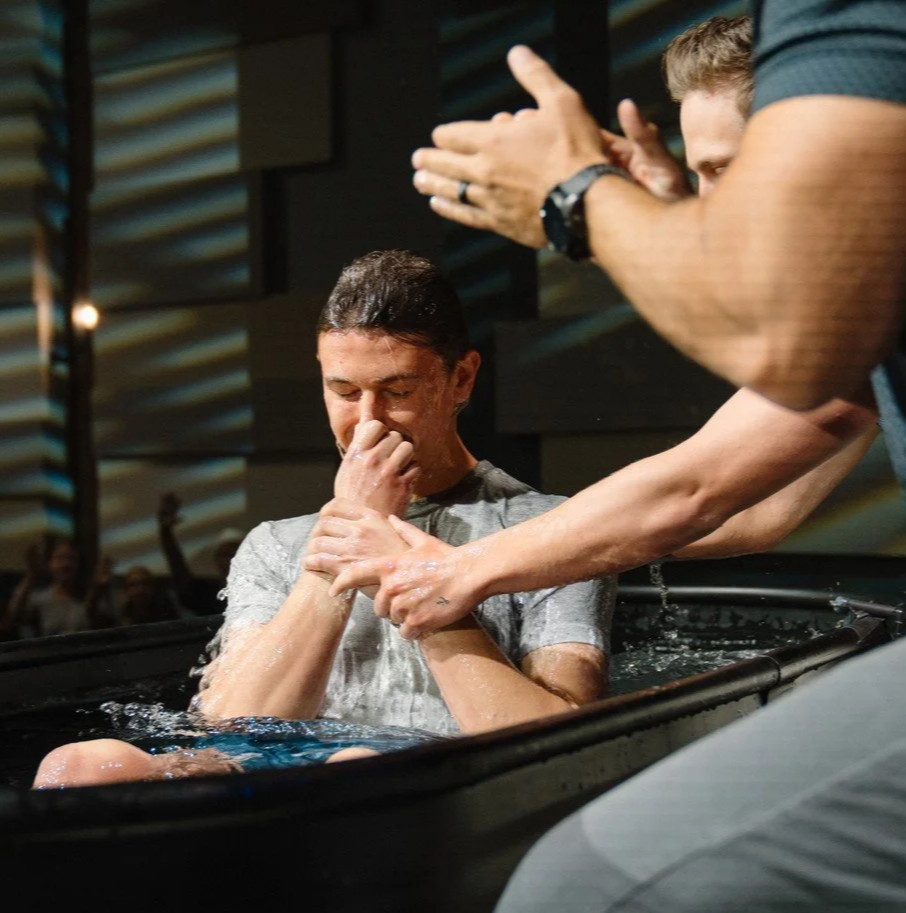 A man baptized in a church by a person whose hands are visibly clapping.