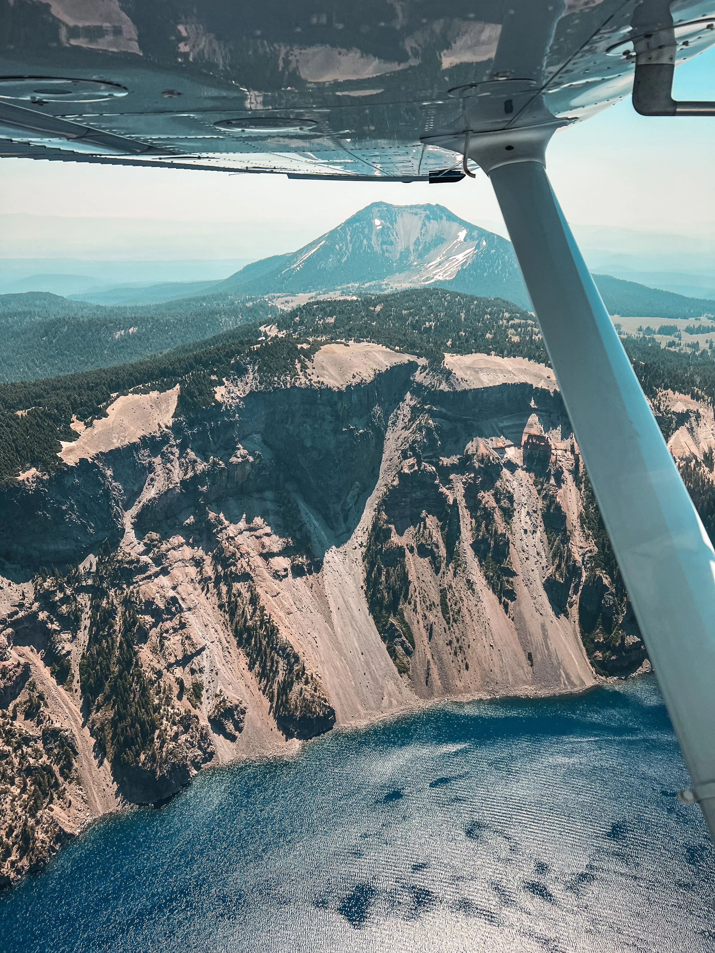 Aerial view of Crater Lake with steep cliffs and blue water, taken from a small airplane flying overhead.