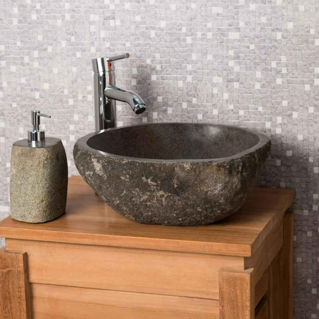 A modern bathroom sink setup with a stone basin on a wooden vanity, a soap dispenser, and a sleek chrome faucet against a textured tiled wall background.