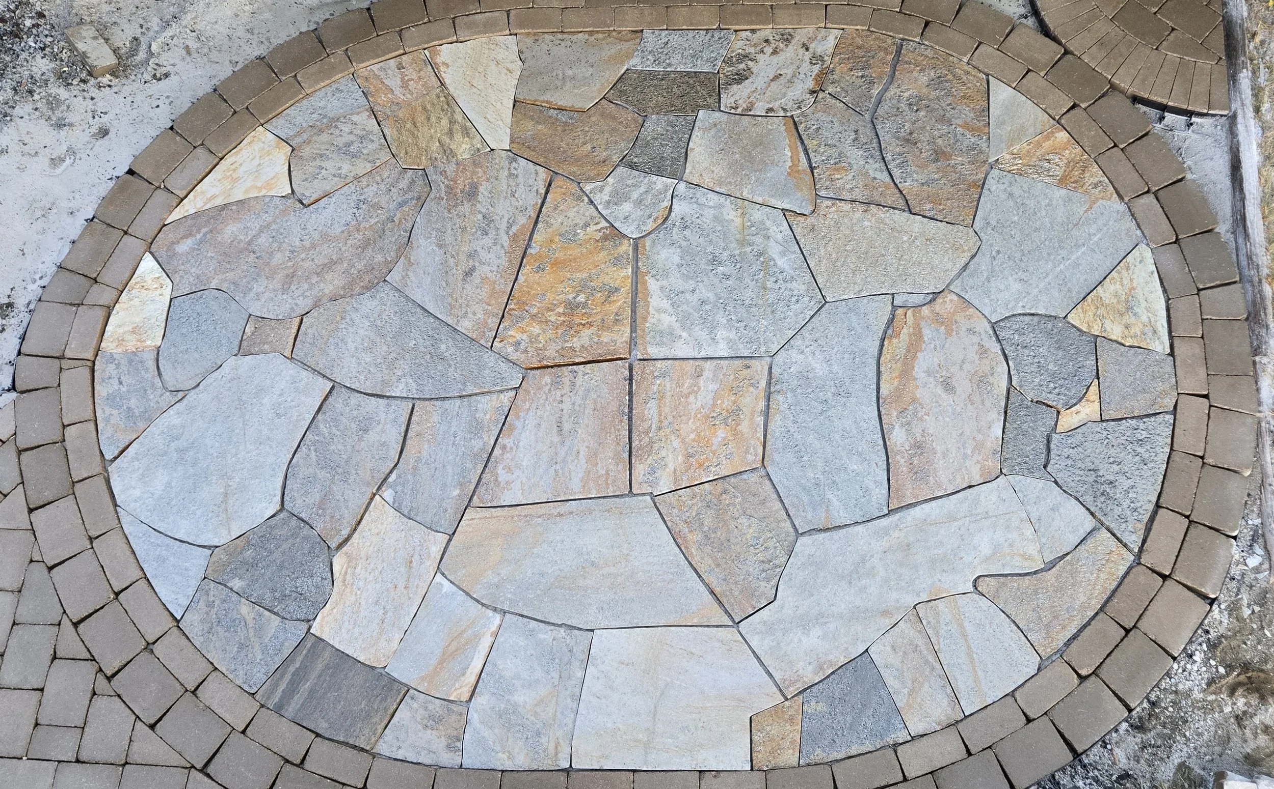 Close-up view of a decorative stone circle with various shapes and colors of stones surrounded by small brick pavers.